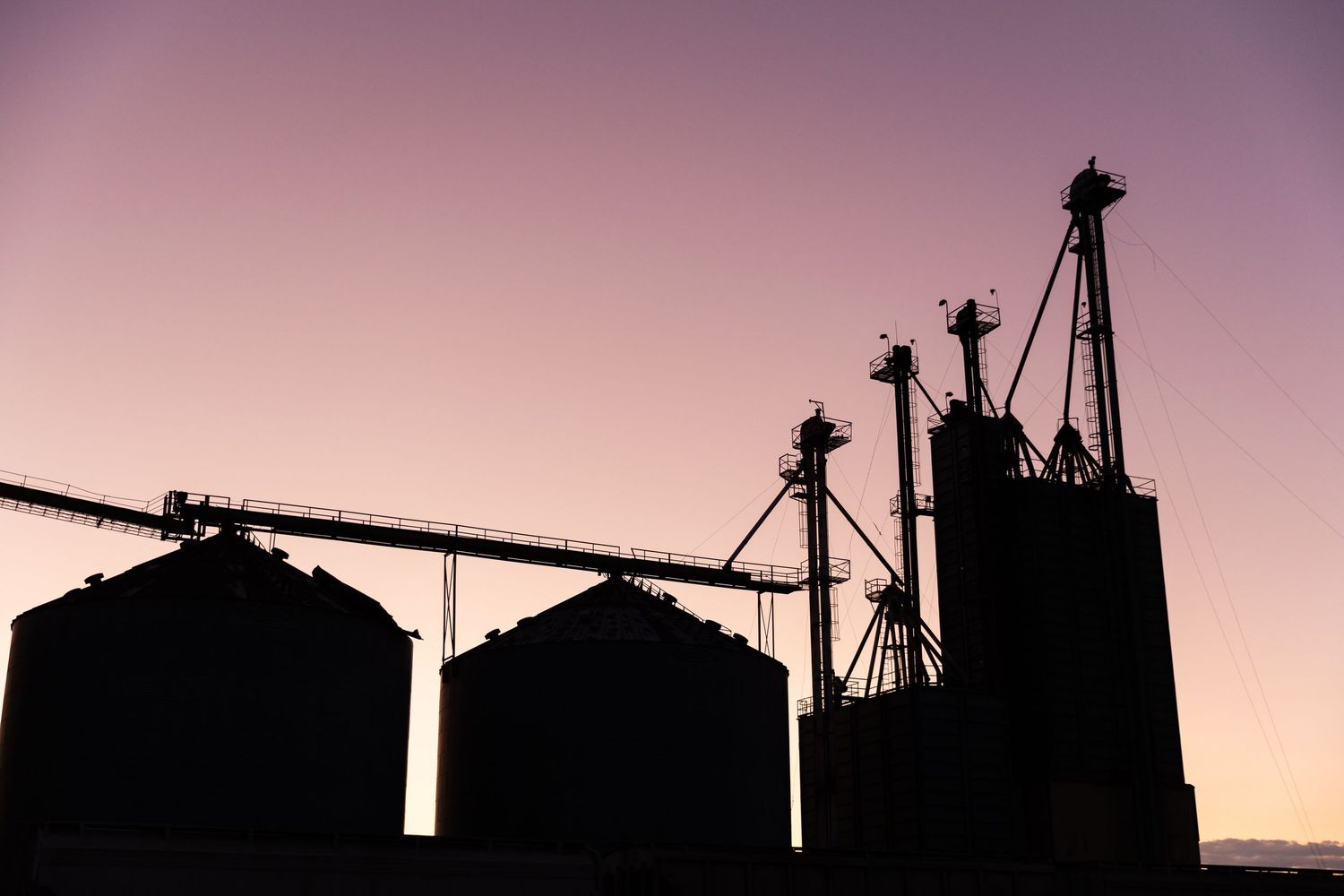 Silhouette of grain silos and industrial elevator equipment against a purple and pink dusk sky.