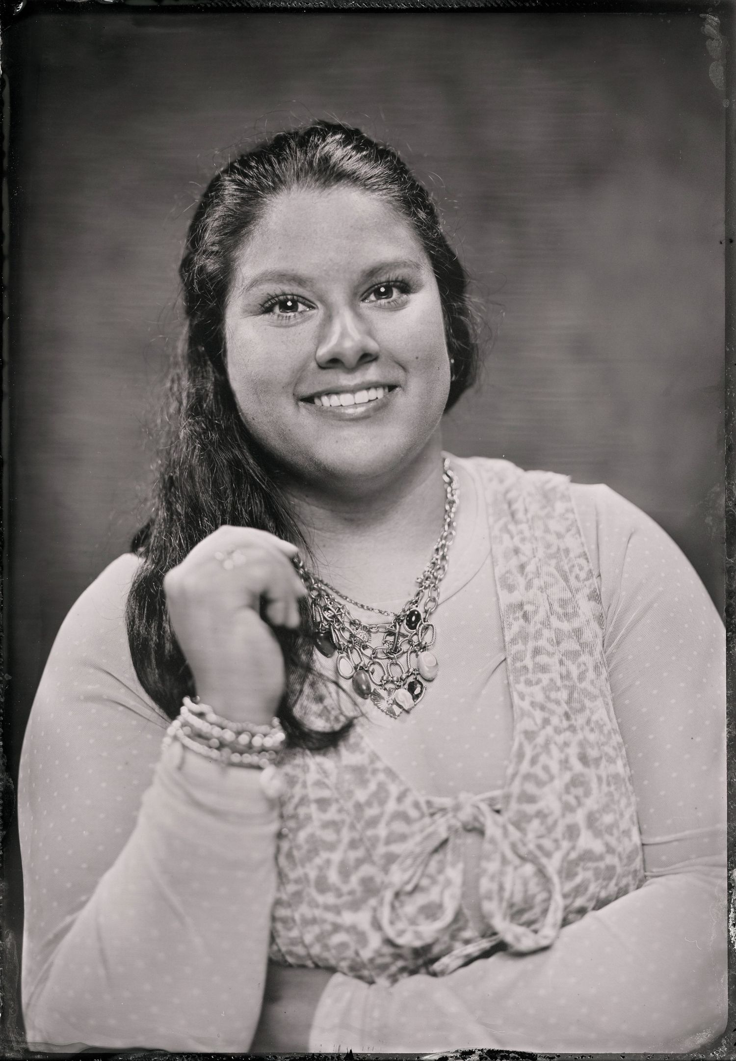 Black and white portrait of a smiling young woman wearing a necklace and bracelet, posing with hands clasped.