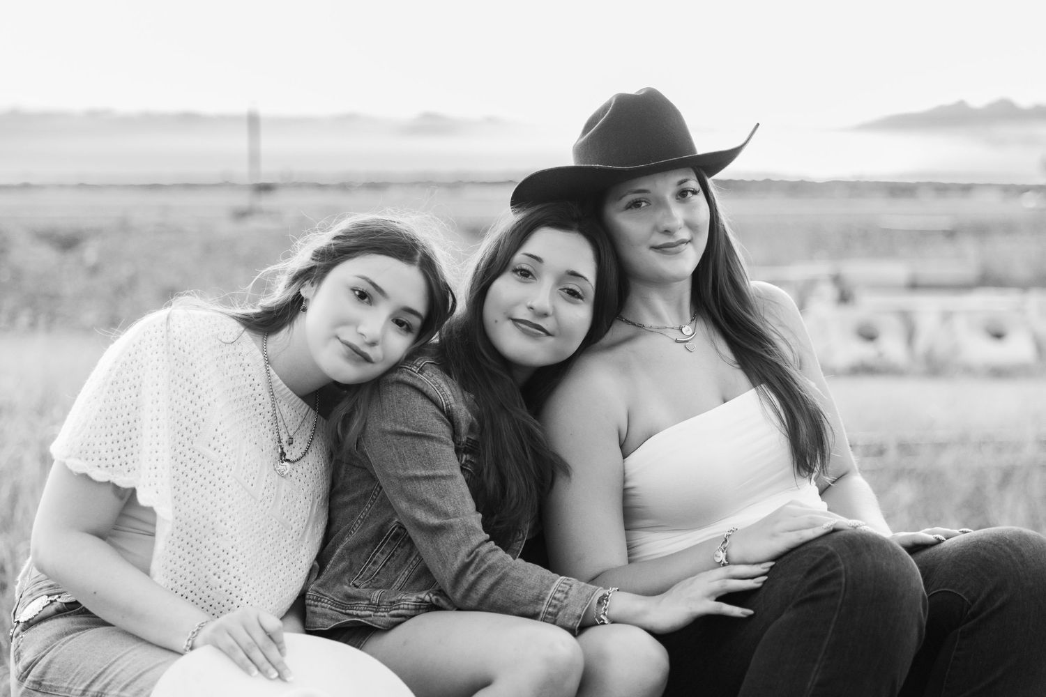 Three young women pose together outdoors in a black and white portrait, one wearing a cowboy hat.