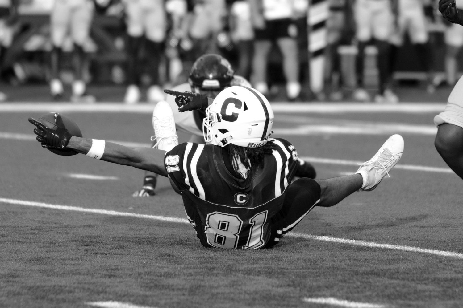 Black and white photo of football player #81 sliding on field with arms outstretched during a game.