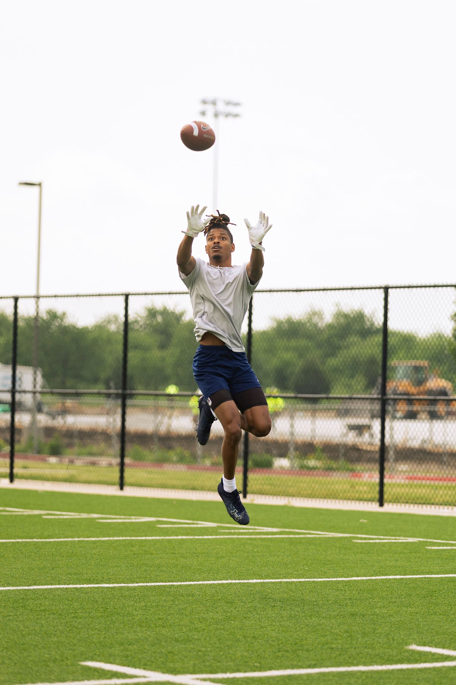 Athletic football player leaping to catch a pass on green turf field during outdoor practice session.