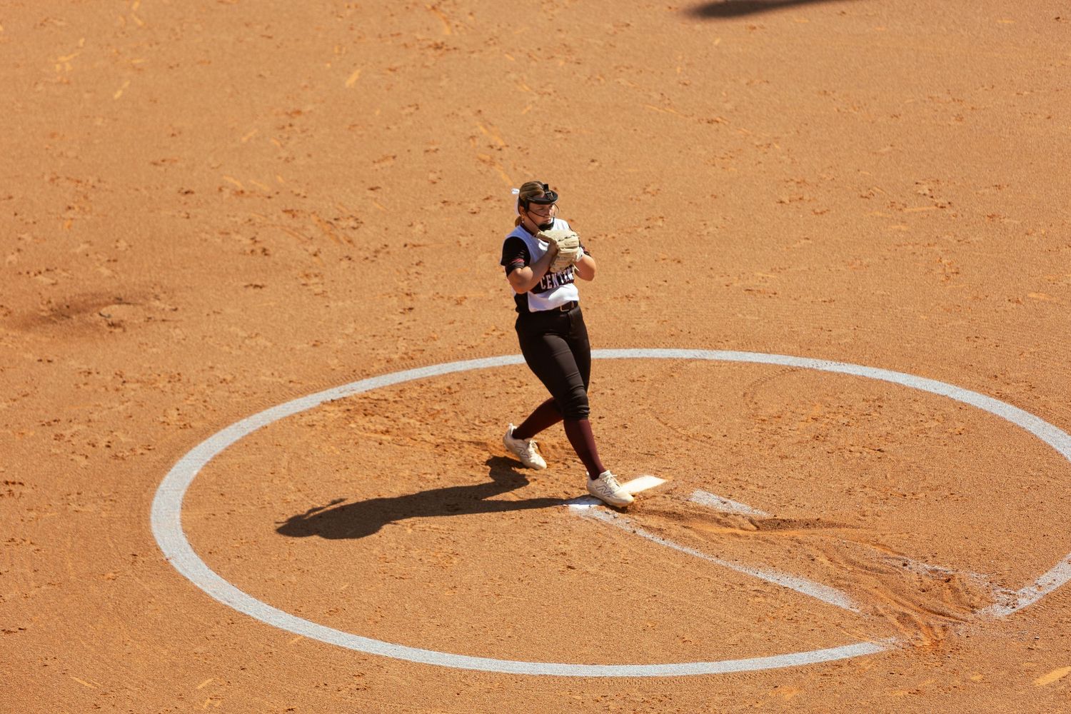 Female softball pitcher winding up on a clay pitcher's mound during a game.