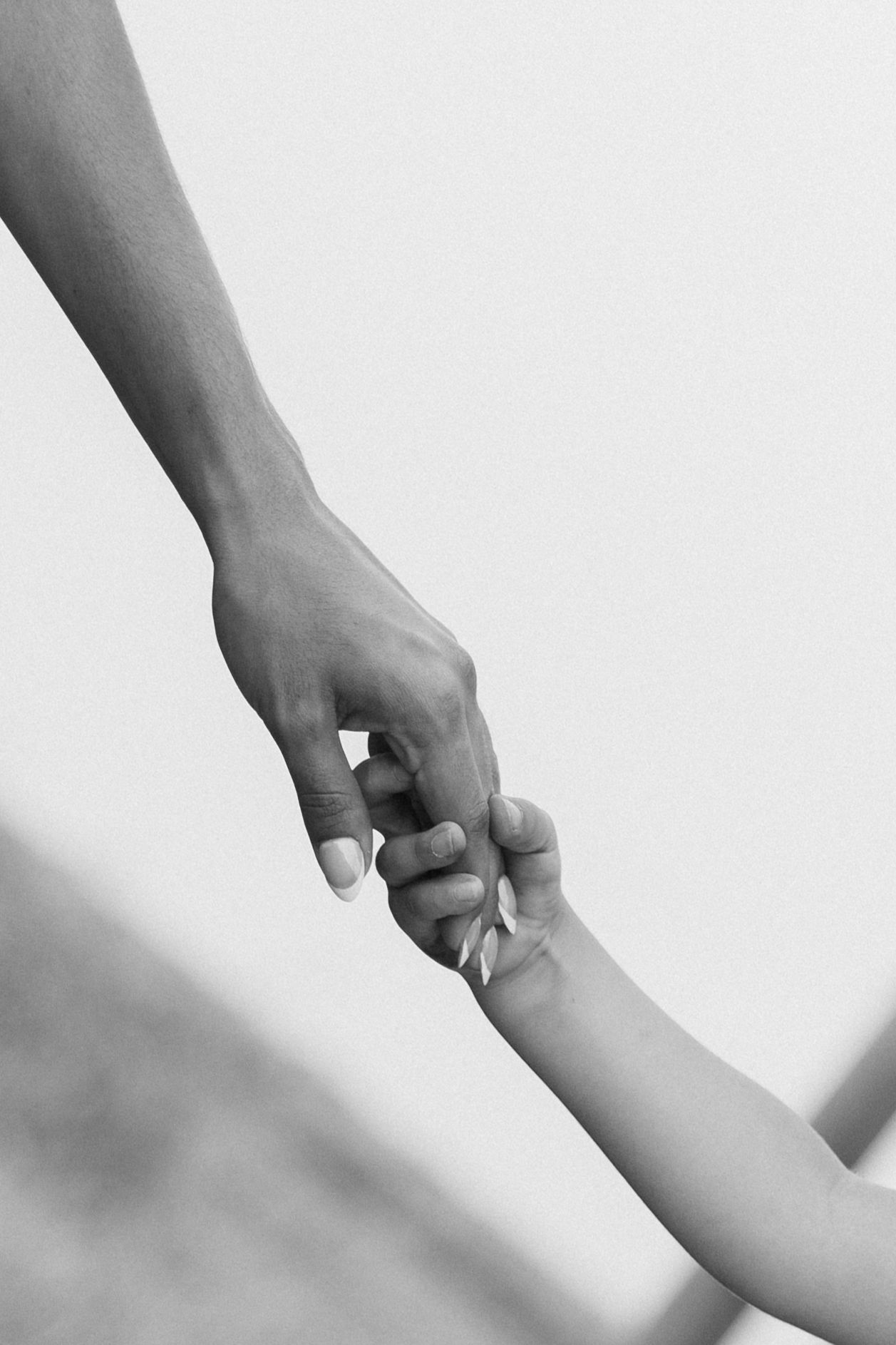 Black and white photo of an adult hand gently holding a small child's hand, symbolizing love and care.