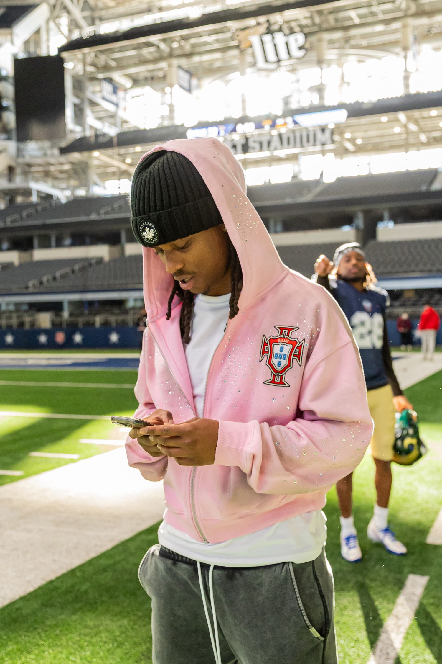Young man in pink Portugal hoodie checks his phone on the field at AT&T Stadium.