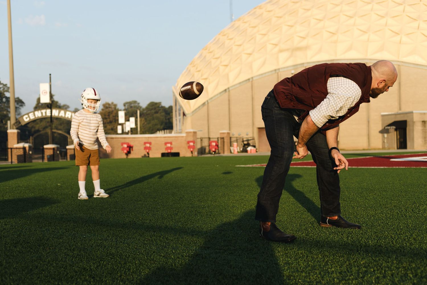 Father and young son playing football on a college athletic field at sunset.