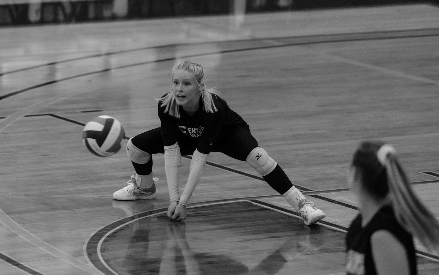 Black and white photo of a blonde volleyball player diving to receive the ball during a match.