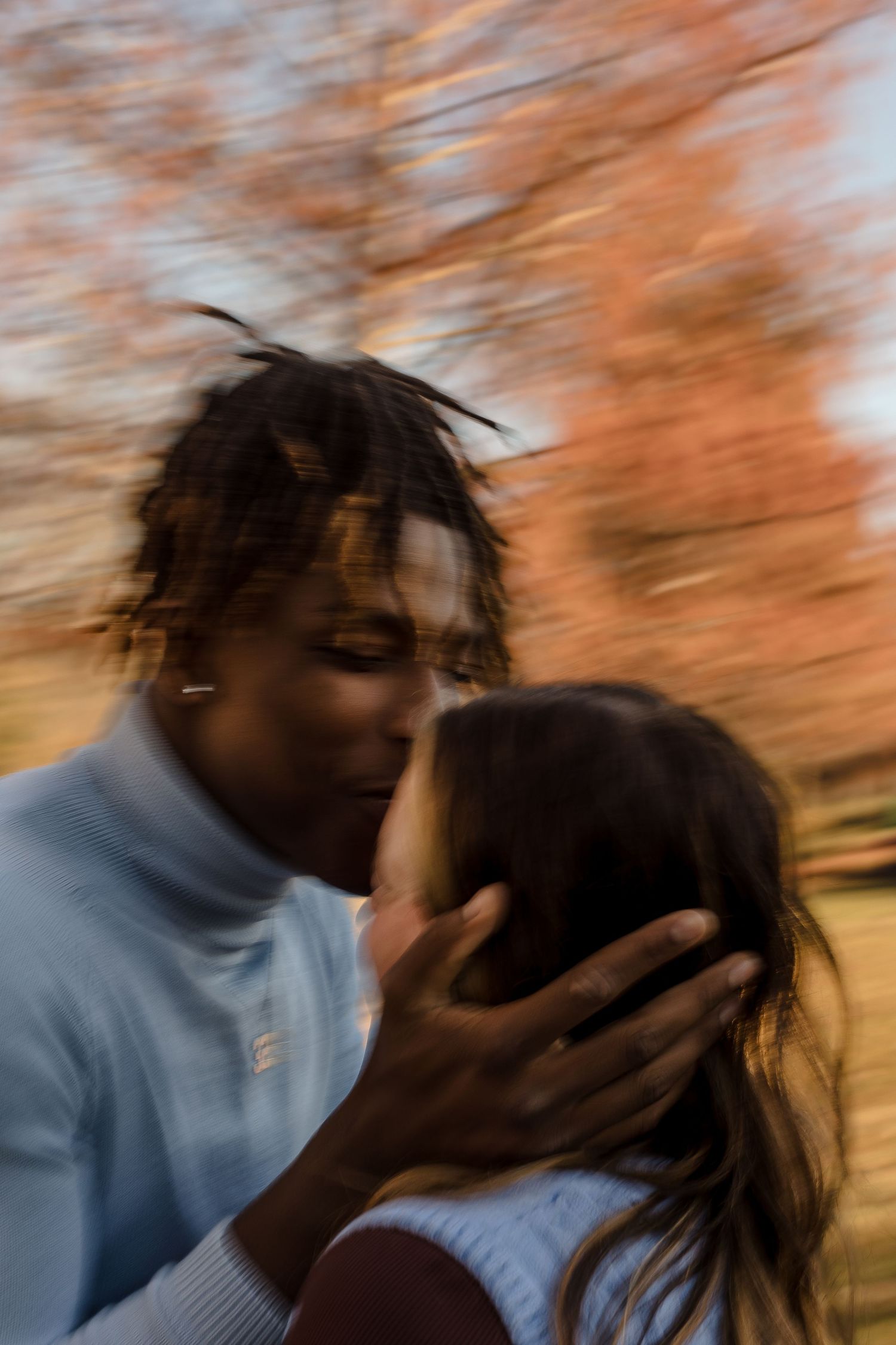 Blurred motion photo of a man kissing a woman on the forehead in an autumn outdoor setting.