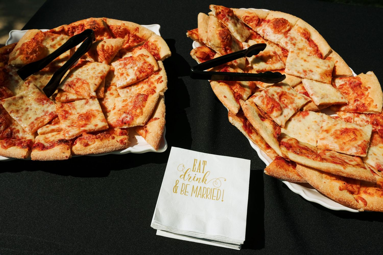 Two sliced pizzas on a table with a napkin reading Eat Drink and Be Married at a wedding.