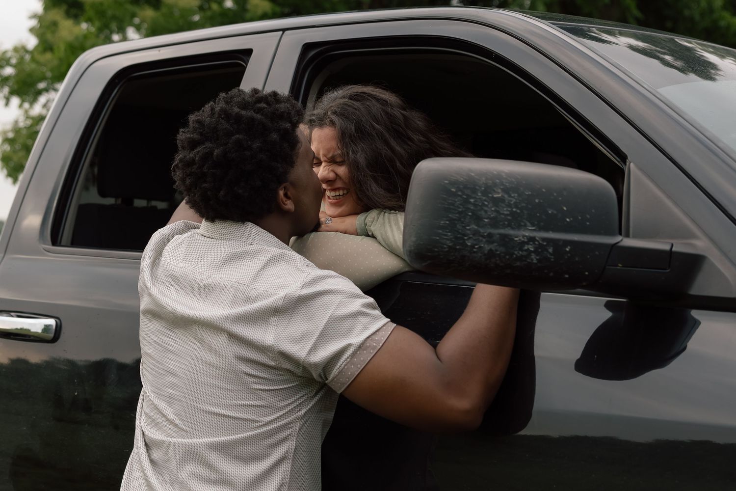 Two people sharing a warm embrace near a gray pickup truck outdoors.