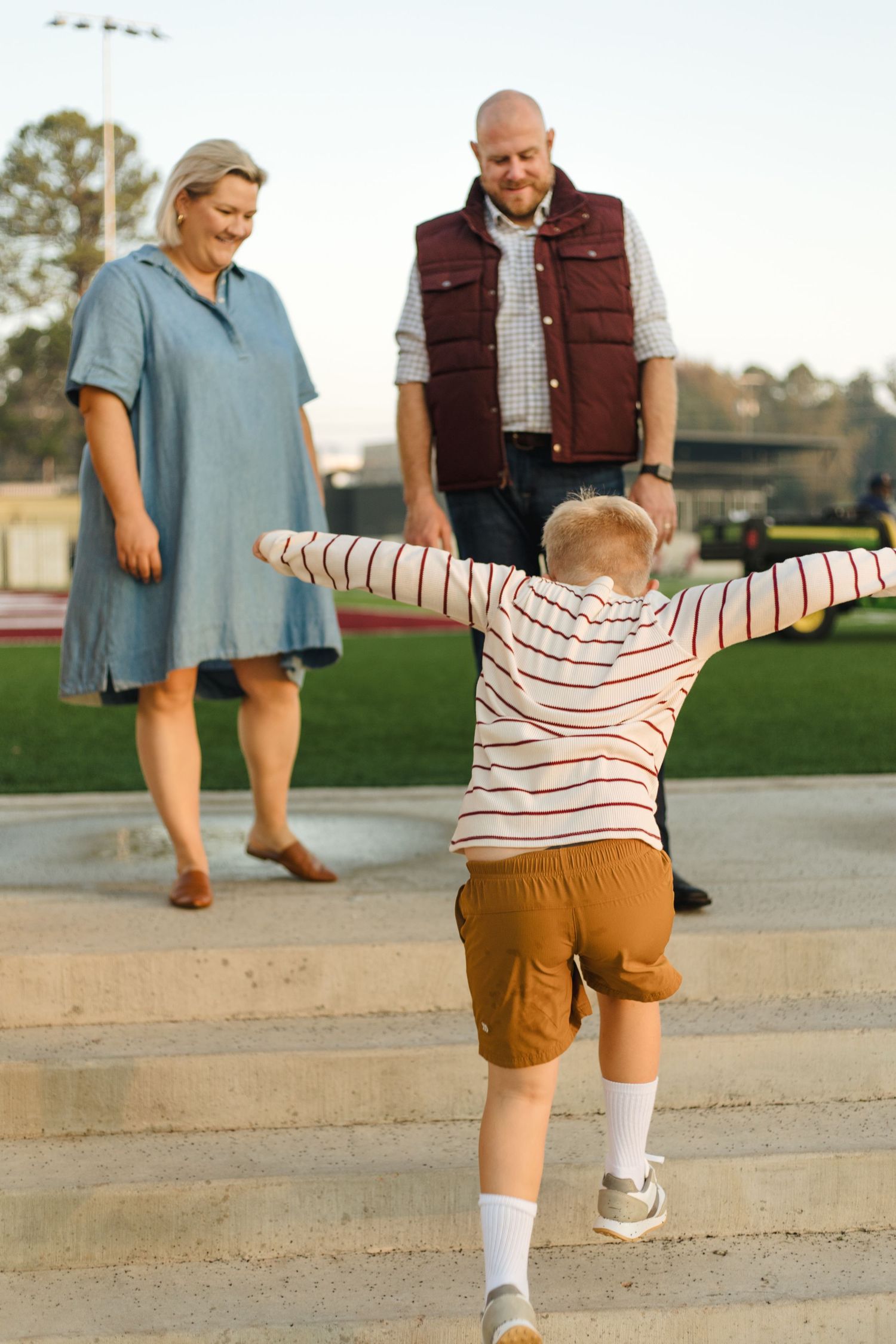 Young boy runs with arms outstretched toward his smiling parents on stadium steps.