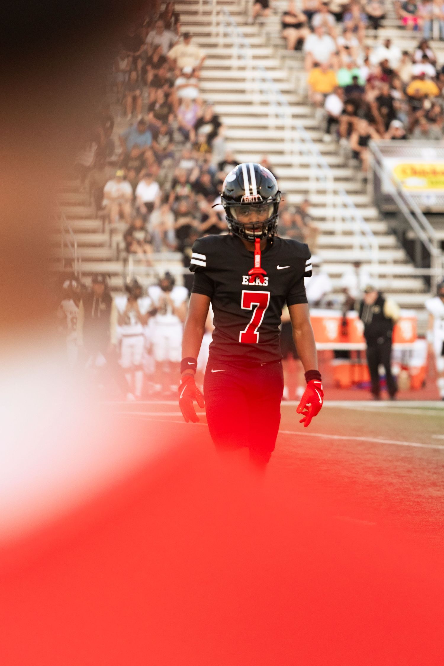 Football player wearing number 7 black jersey walking on field with dramatic red lighting effect.
