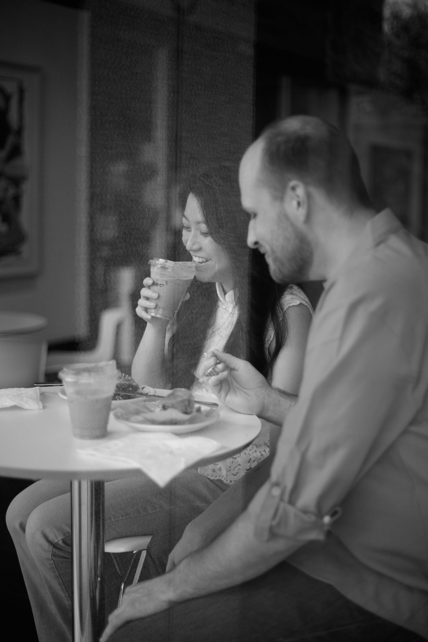 Couple laughing together inside a cozy coffee shop during a relaxed, documentary-style engagement session.