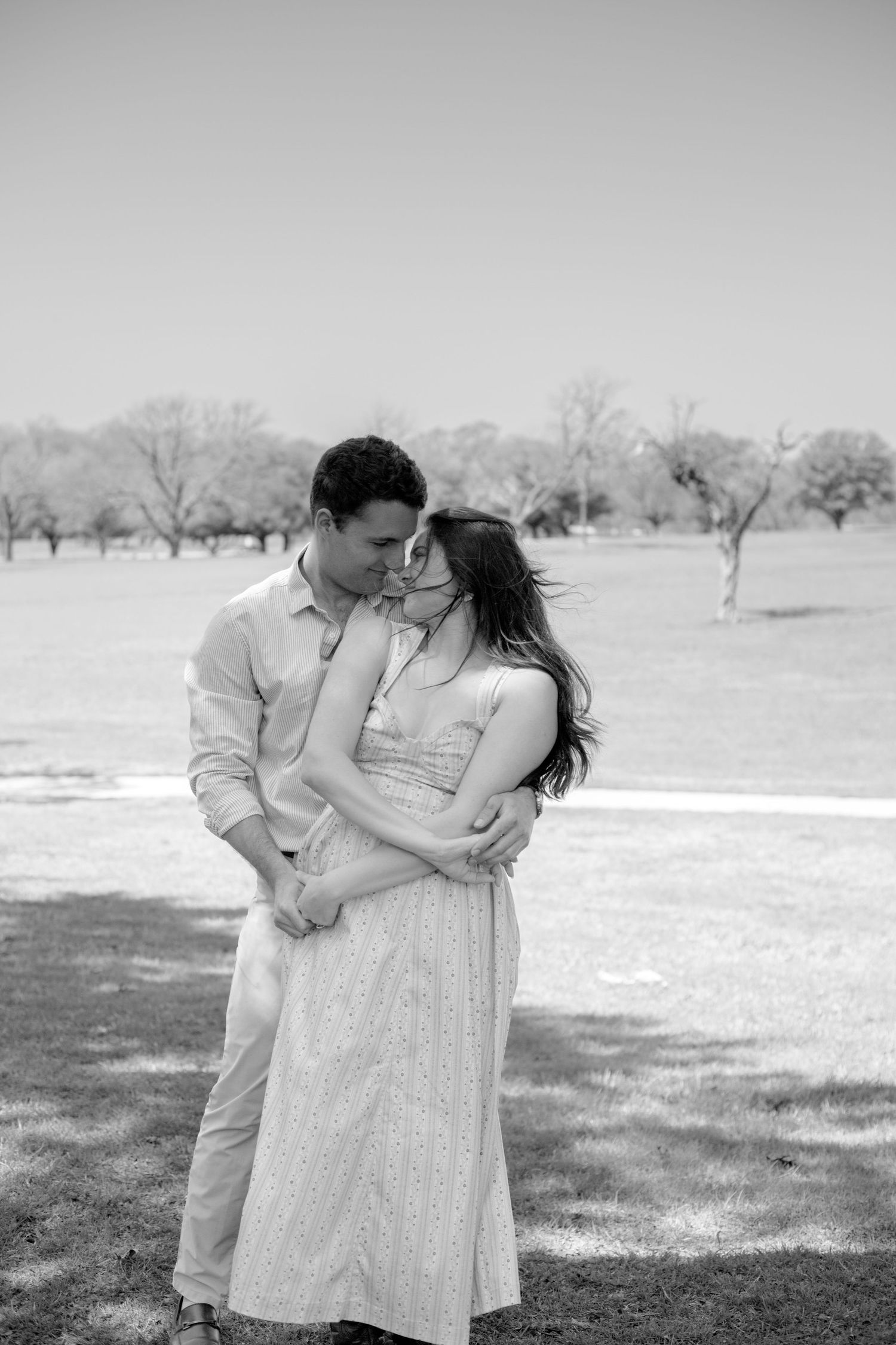 Engaged couple standing nose to nose while embracing in an open field during a candid documentary-style engagement session.
