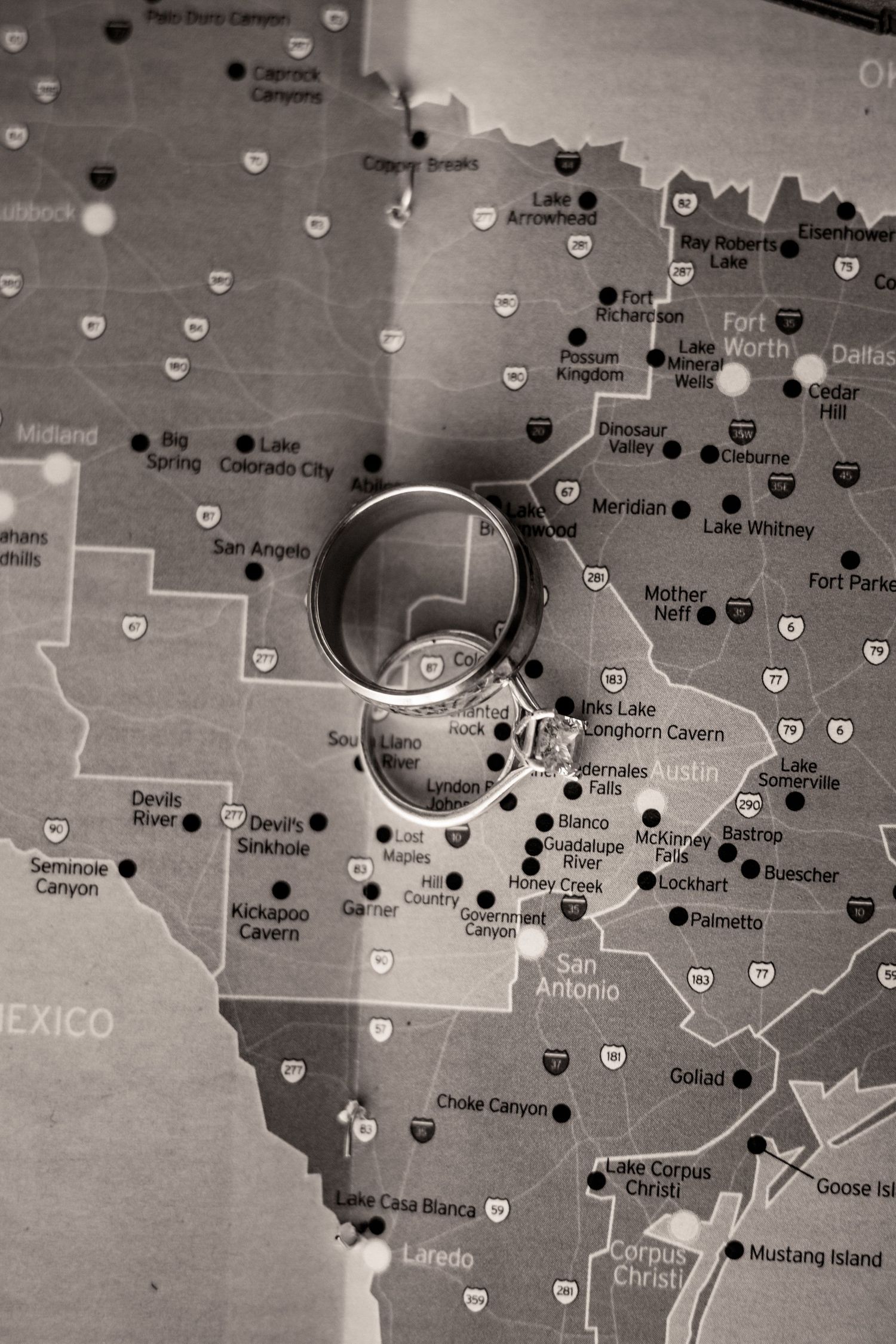 Close-up of wedding rings resting on a map of the Texas Hill Country and Central Texas, symbolizing the couple's wedding destination.