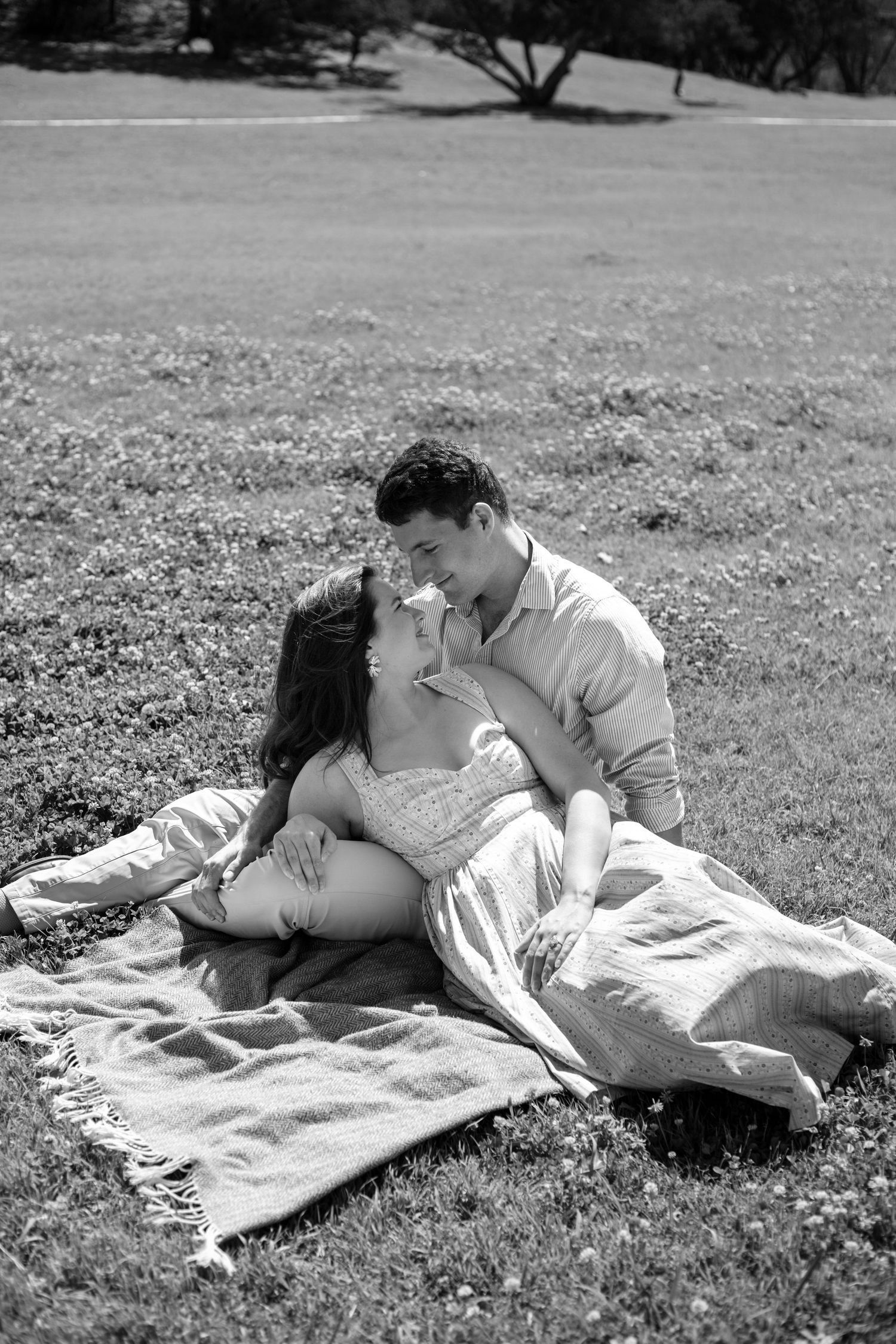 Engaged couple relaxing together on a picnic blanket during a candid engagement session at a local park.