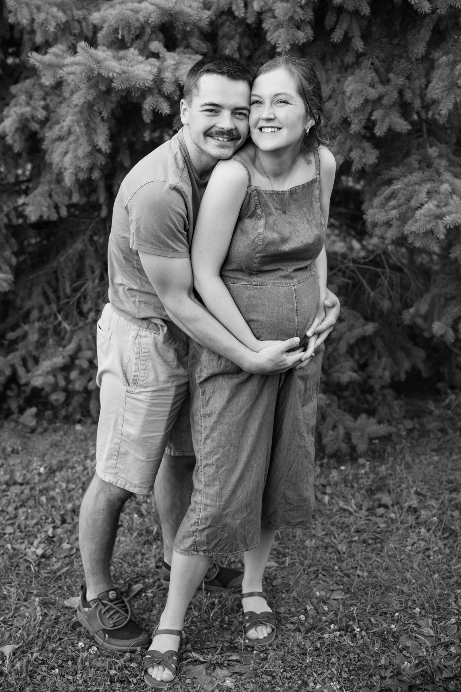 A happy couple embraces outdoors in black and white, with the woman leaning back into the mans arms.