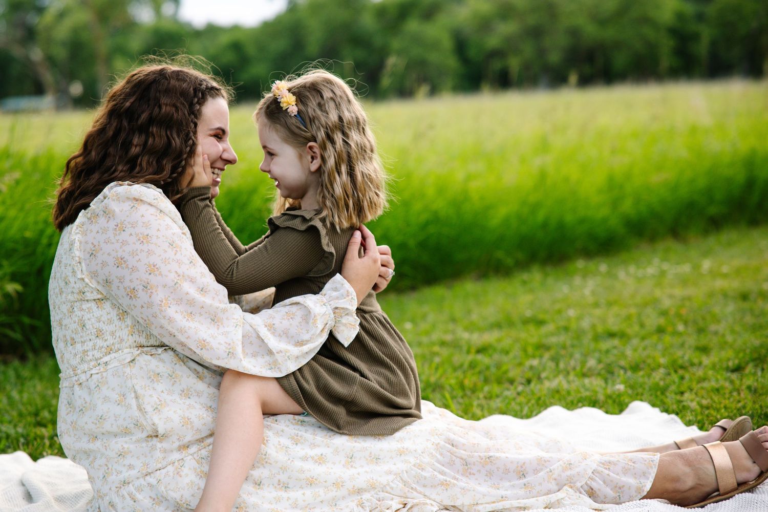 Mother and young daughter sharing a joyful moment sitting together on a blanket in a green meadow.