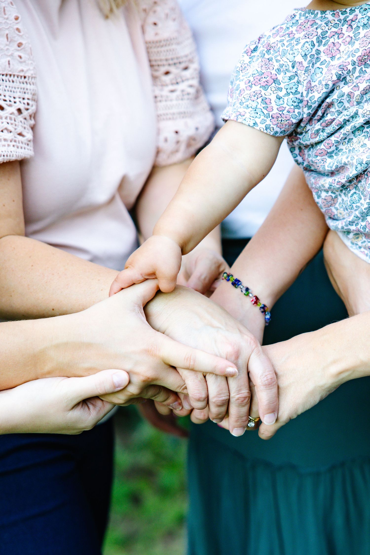 Close-up of four people joining hands together in a circle symbolizing unity and togetherness.