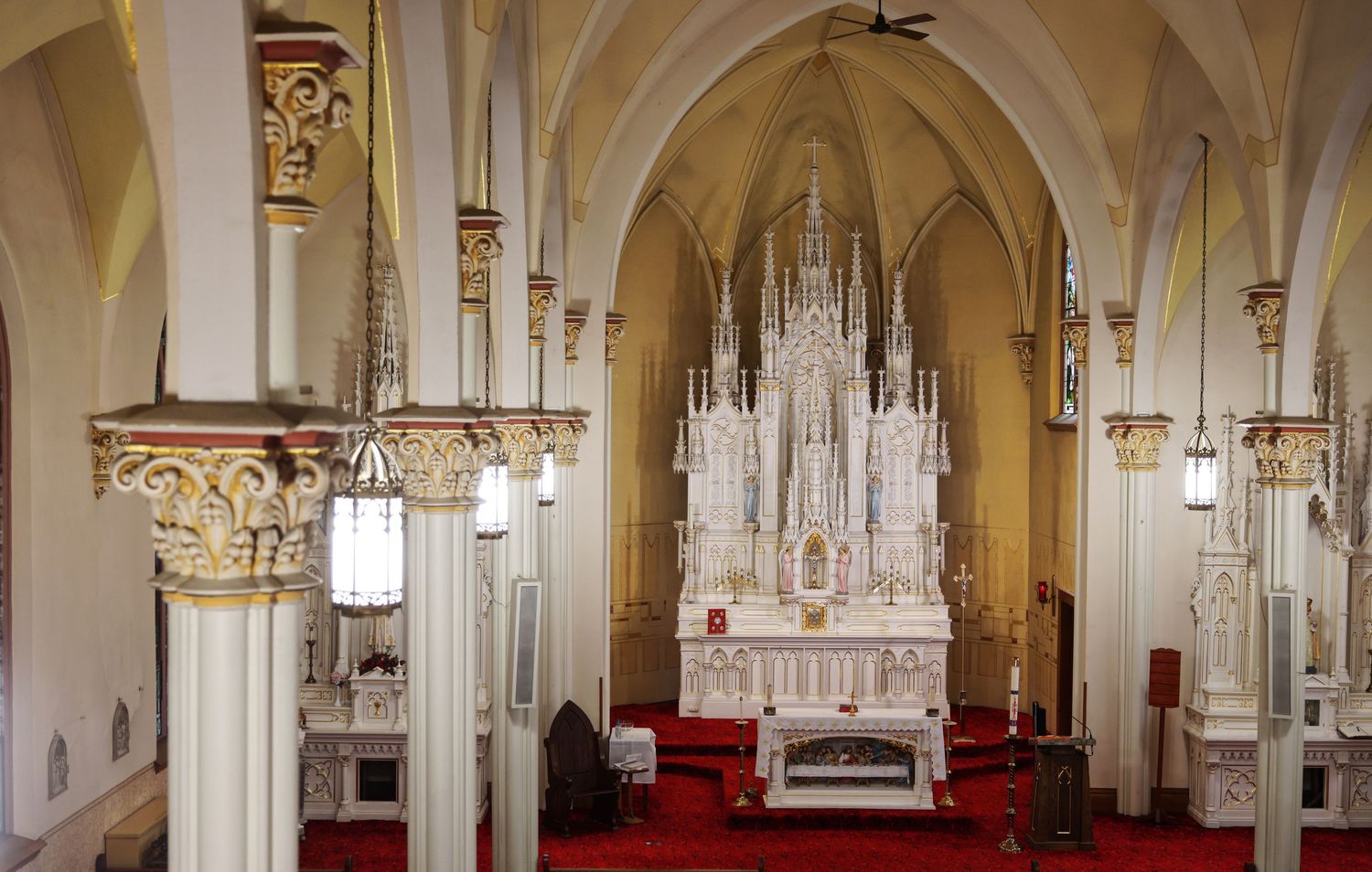 Ornate white Gothic altar with red carpet, decorative columns, and pointed arches inside a historic Catholic church interior.