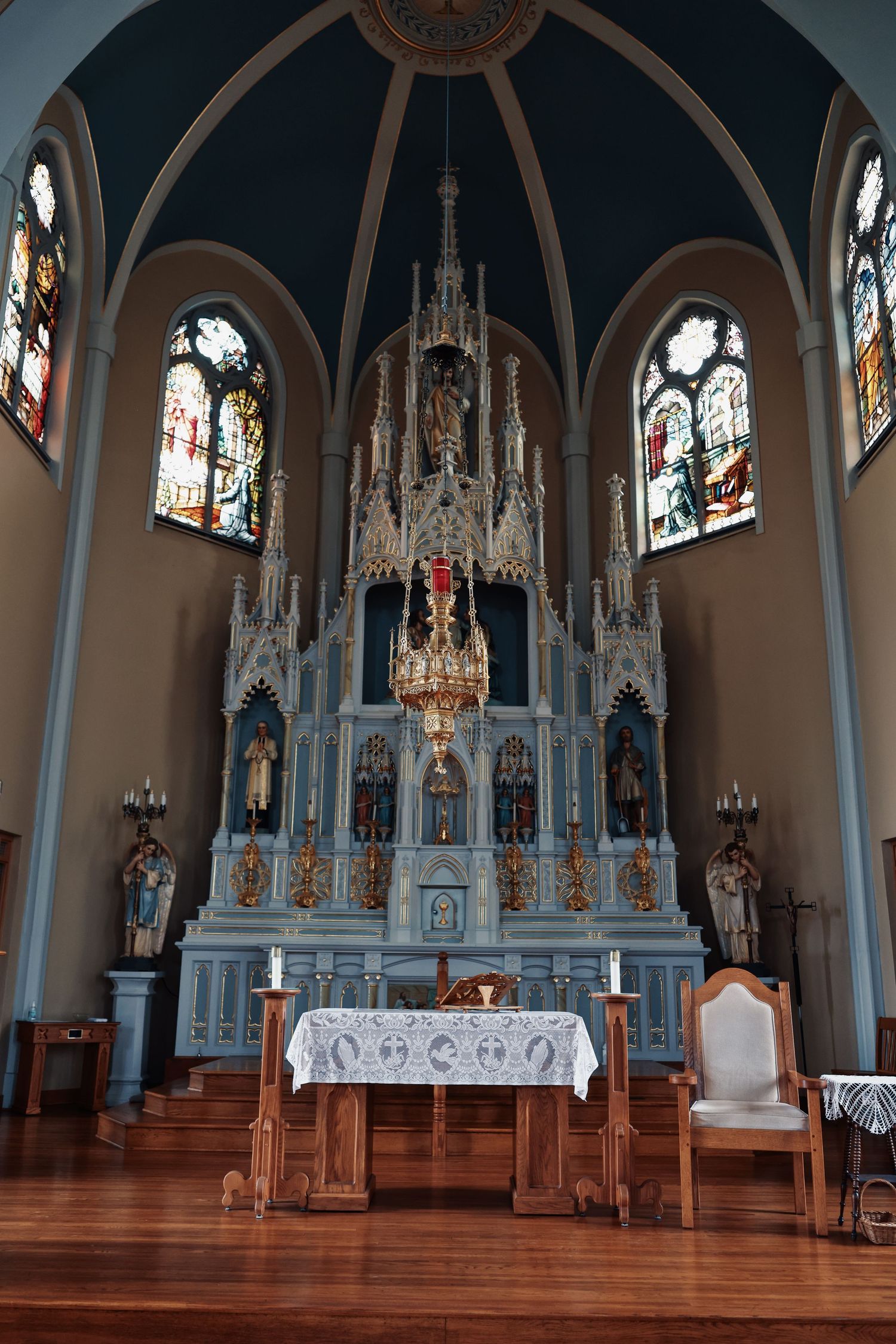 Historic church interior featuring ornate blue altar, stained glass windows, and vaulted ceiling in a Gothic Revival style.