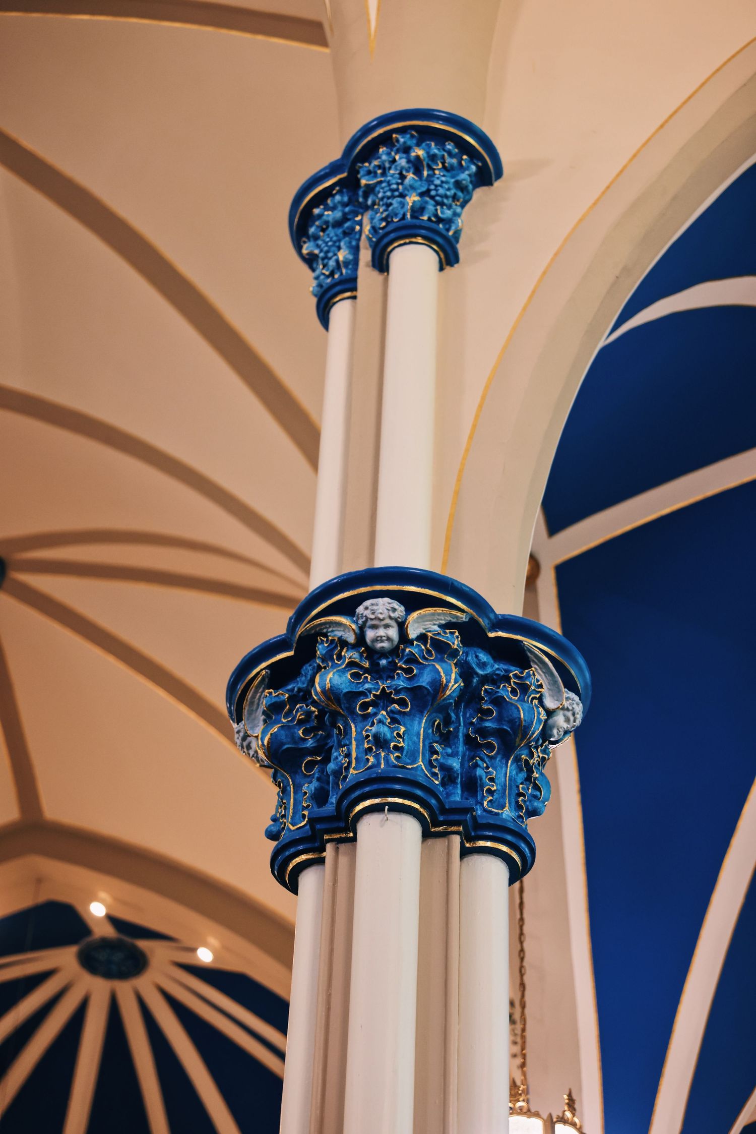 Ornate blue ceramic column capitals with angelic figures in a vaulted architectural interior.