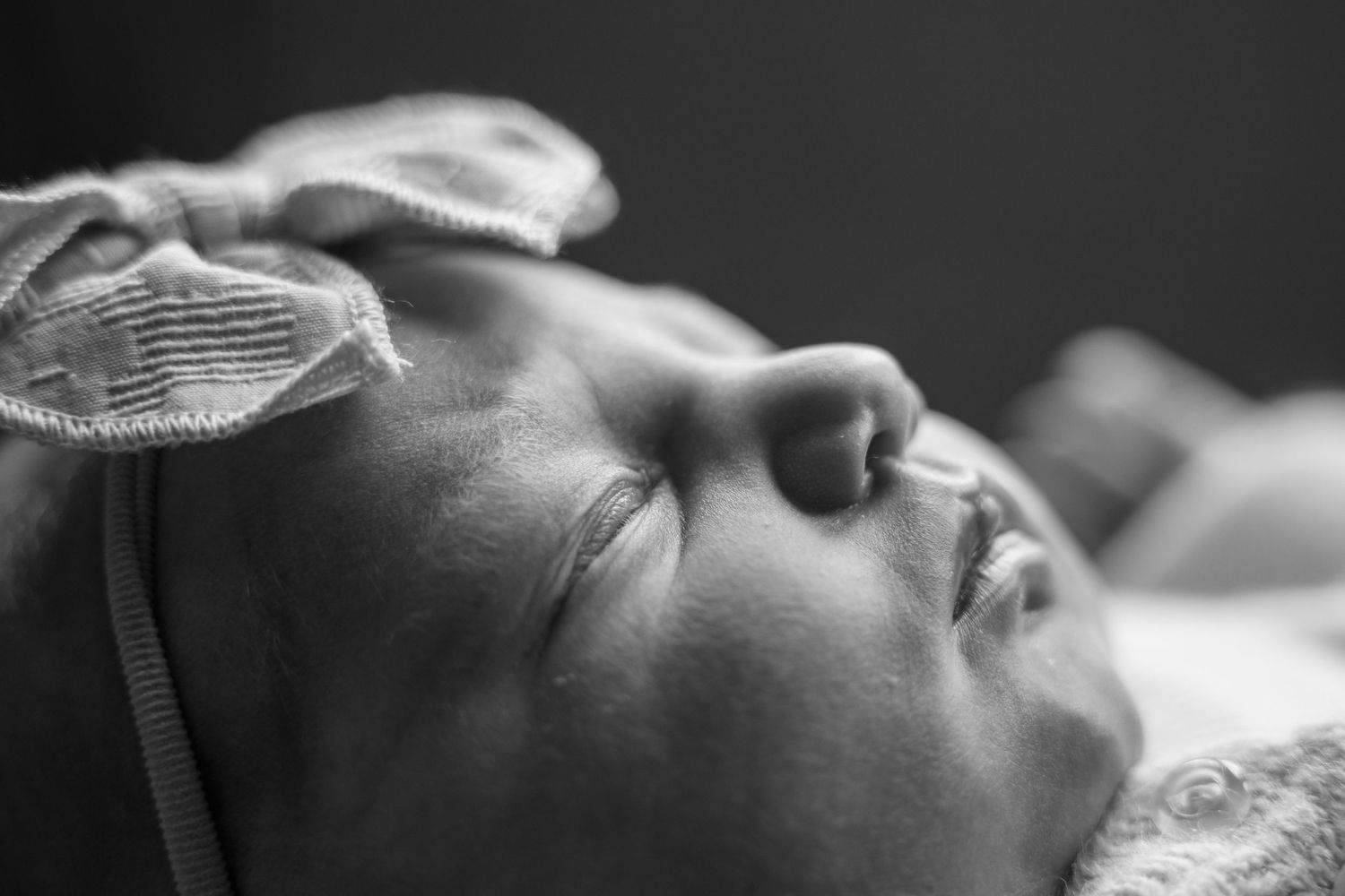 Close-up black and white photo of a sleeping newborn baby wearing a soft headband.