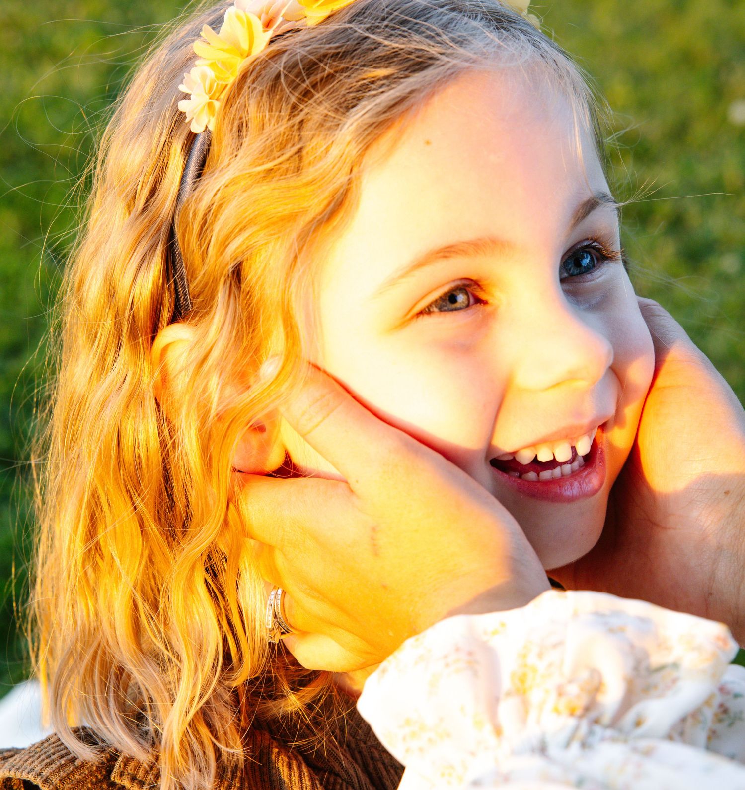 A joyful young girl with a yellow flower clip smiles brightly as hands gently cup her face.