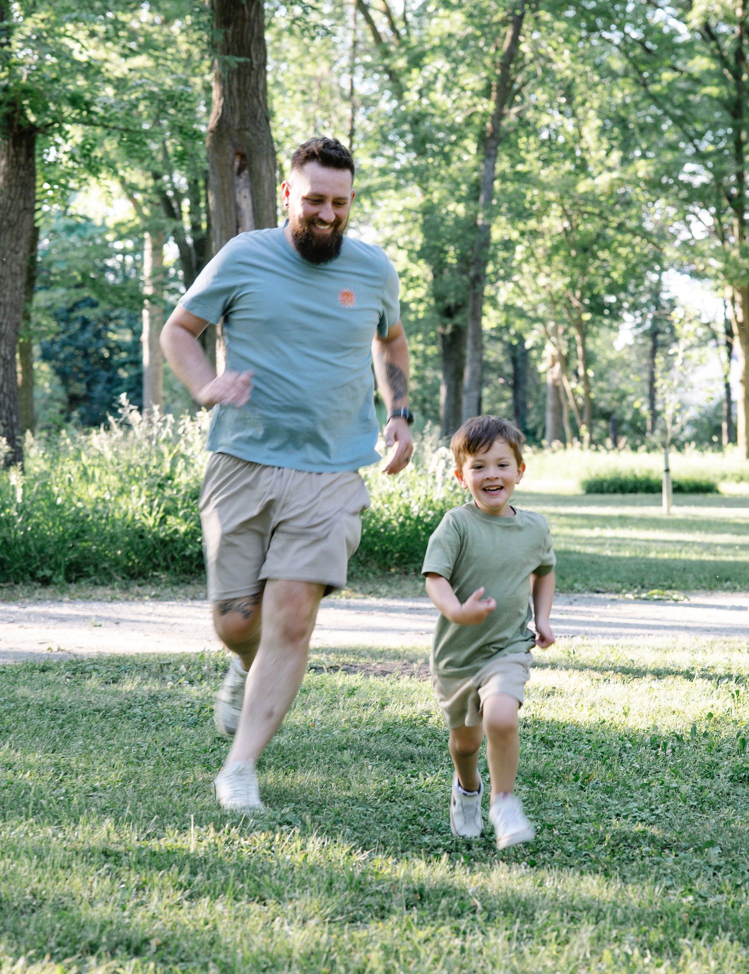 A bearded man and young boy joyfully running together on green grass in a sunny park.