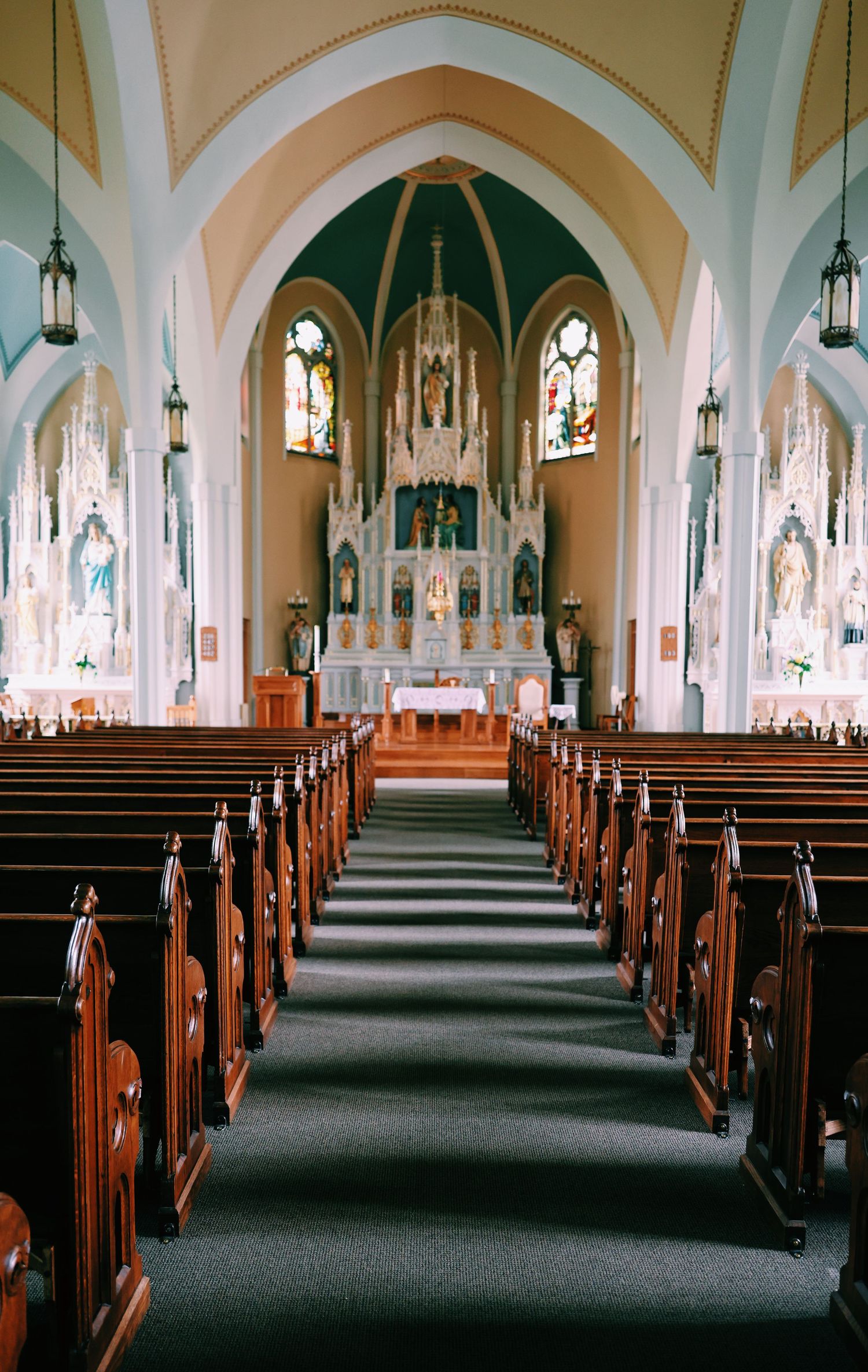 Interior of a grand Catholic church with wooden pews, ornate altar, stained glass windows, and arched ceilings.