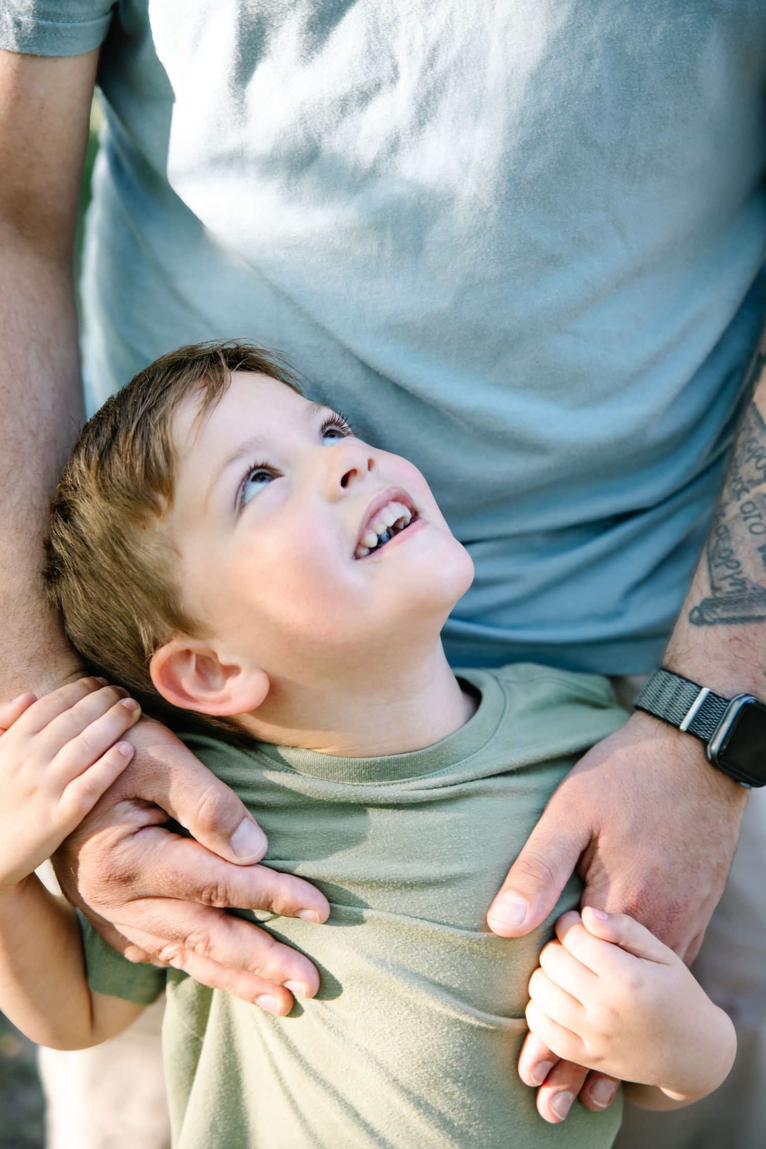 Happy young boy looking up smiling while father holds him gently in an outdoor setting.