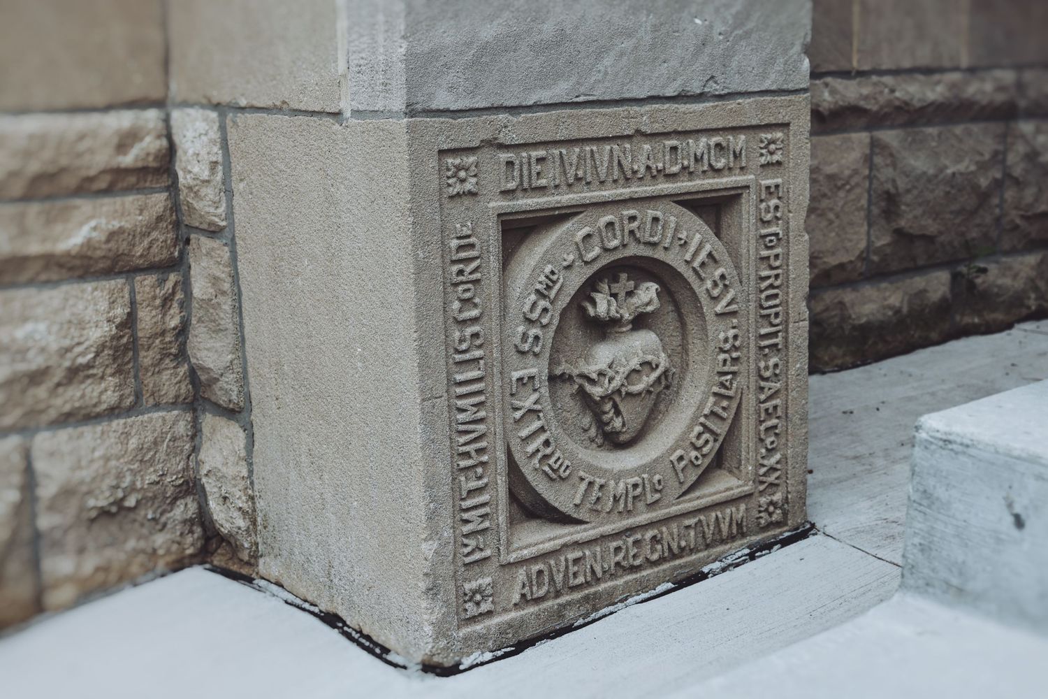 Close-up of an ornate stone cornerstone with carved Latin inscriptions and decorative medallion on a historic building.