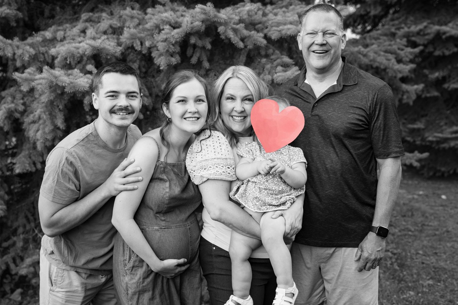 Black and white family photo with four people smiling outdoors, one child holding a red heart balloon.