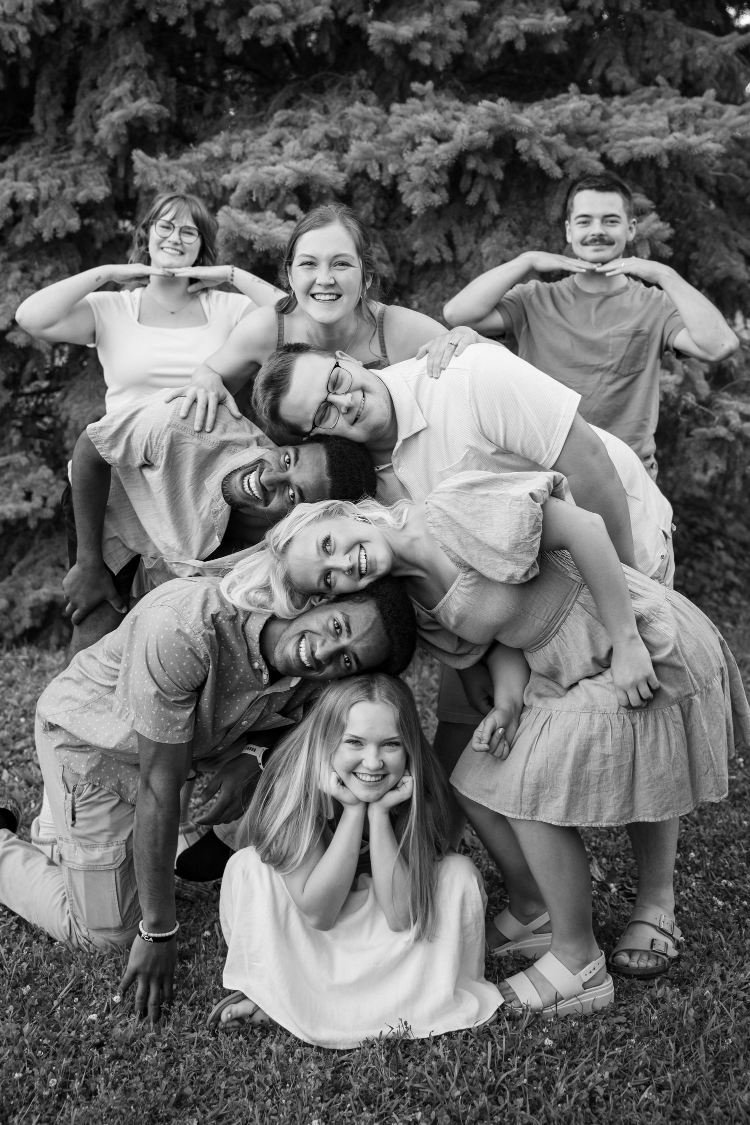A fun black and white photo of a large family group stacking together playfully on a lawn.