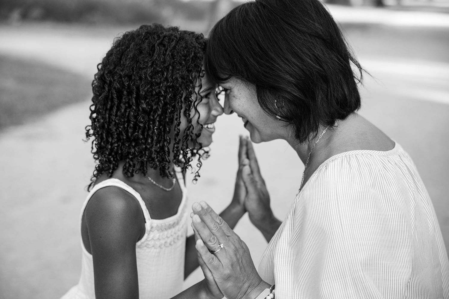 Black and white photo of a mother and daughter touching foreheads, sharing a tender moment outdoors.