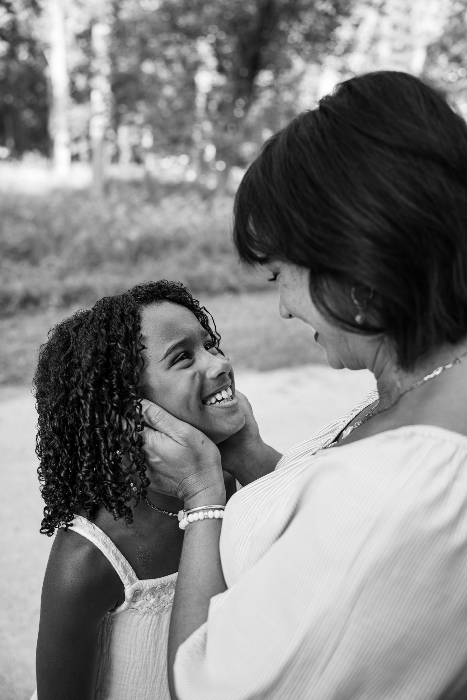 Black and white photo of a woman tenderly cupping a smiling young girl's face outdoors.