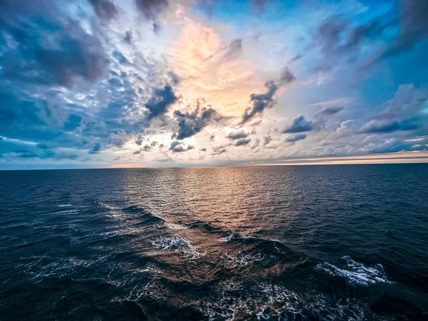 Aerial view of a dramatic sunset over the open ocean with colorful clouds and calm waters.