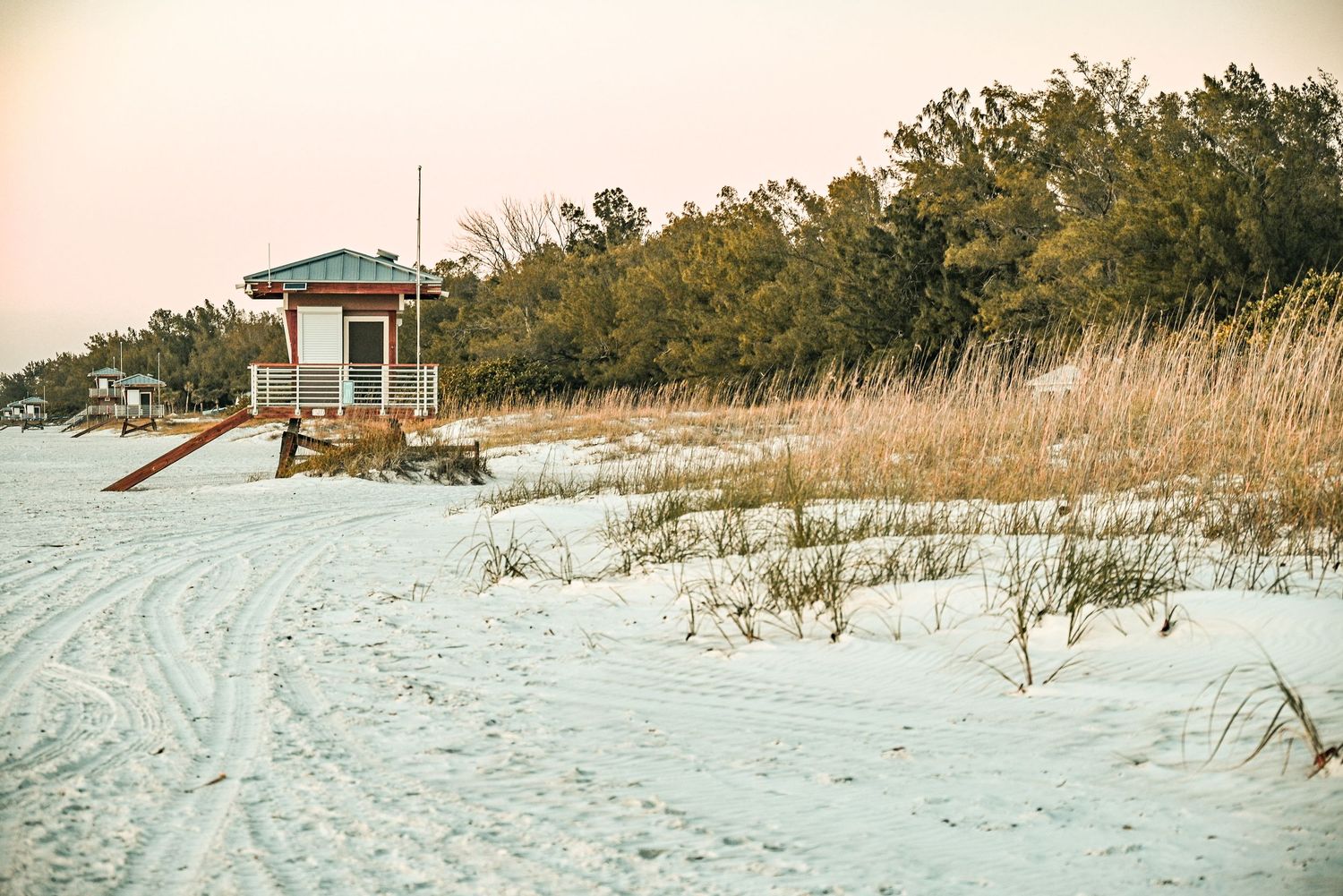 Sandy white beach at sunset with a lifeguard tower and sea grass dunes.