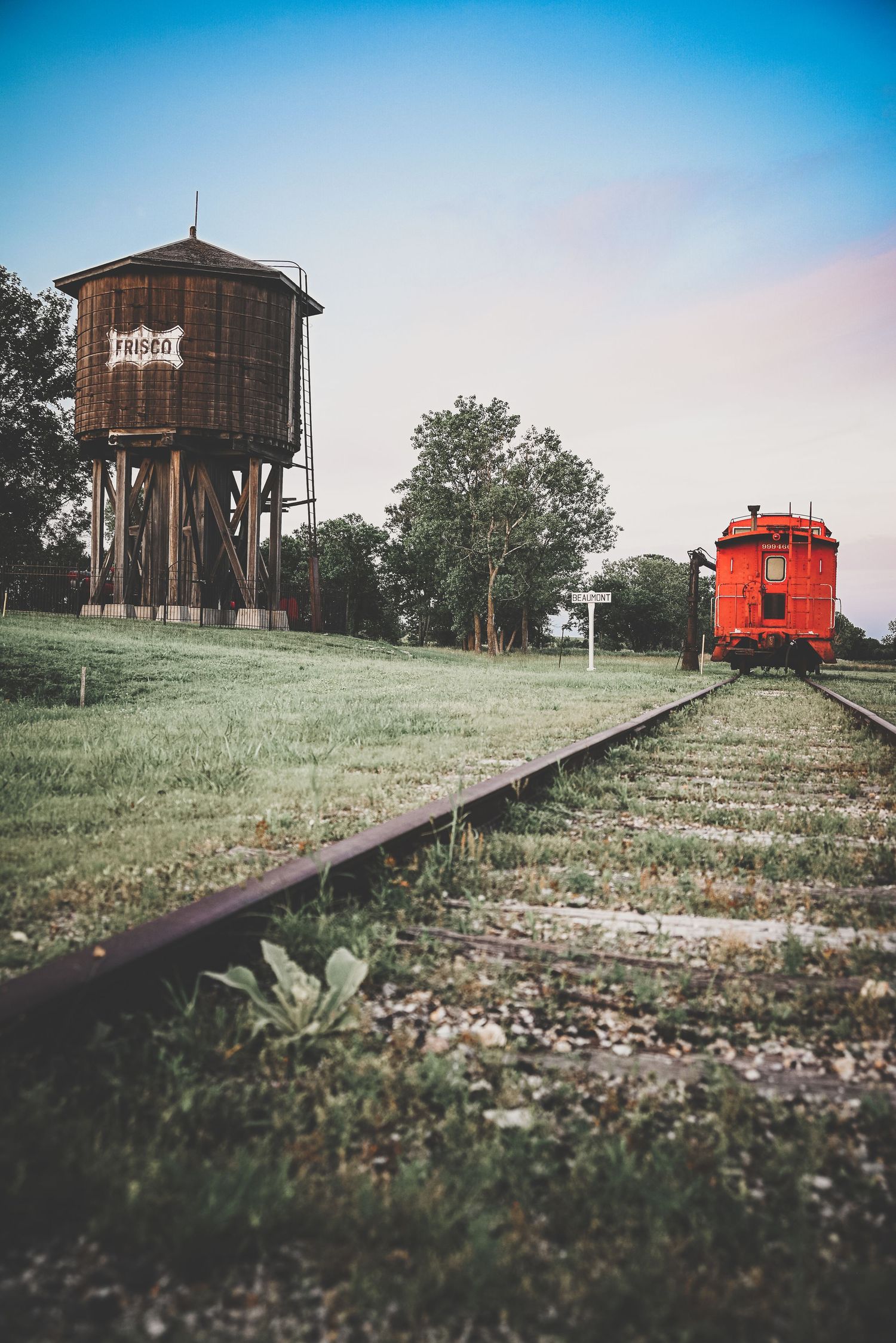 Rustic wooden water tower and red caboose beside old railroad tracks at dusk.
