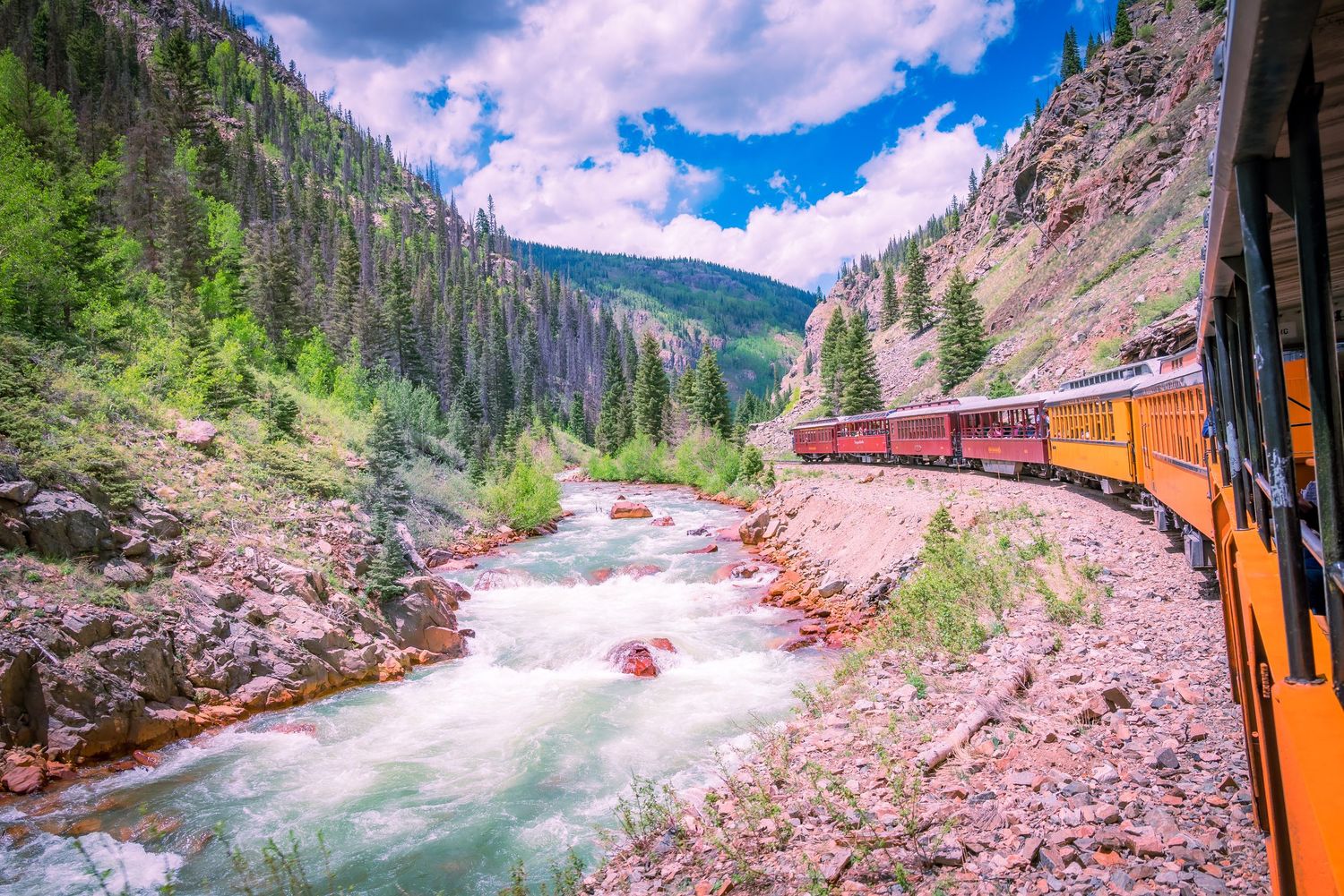 Durango and Silverton Narrow Gauge Railroad train traveling alongside a rushing mountain river.