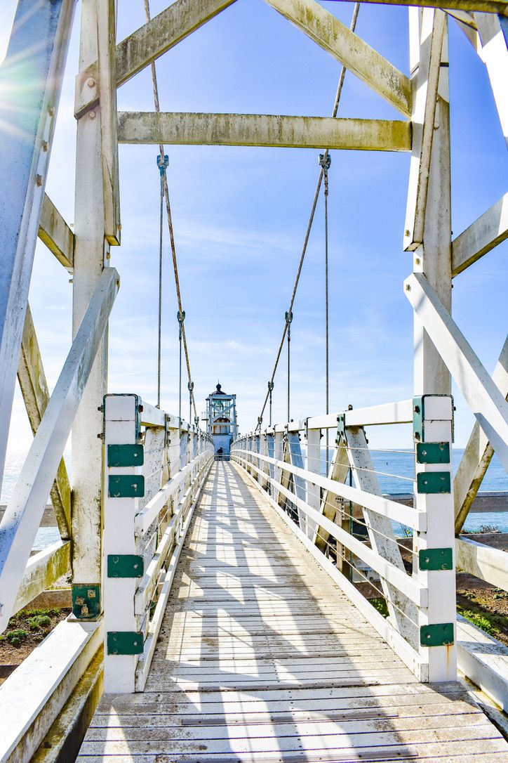 White wooden suspension bridge leading to a lighthouse under a bright blue sky in California.
