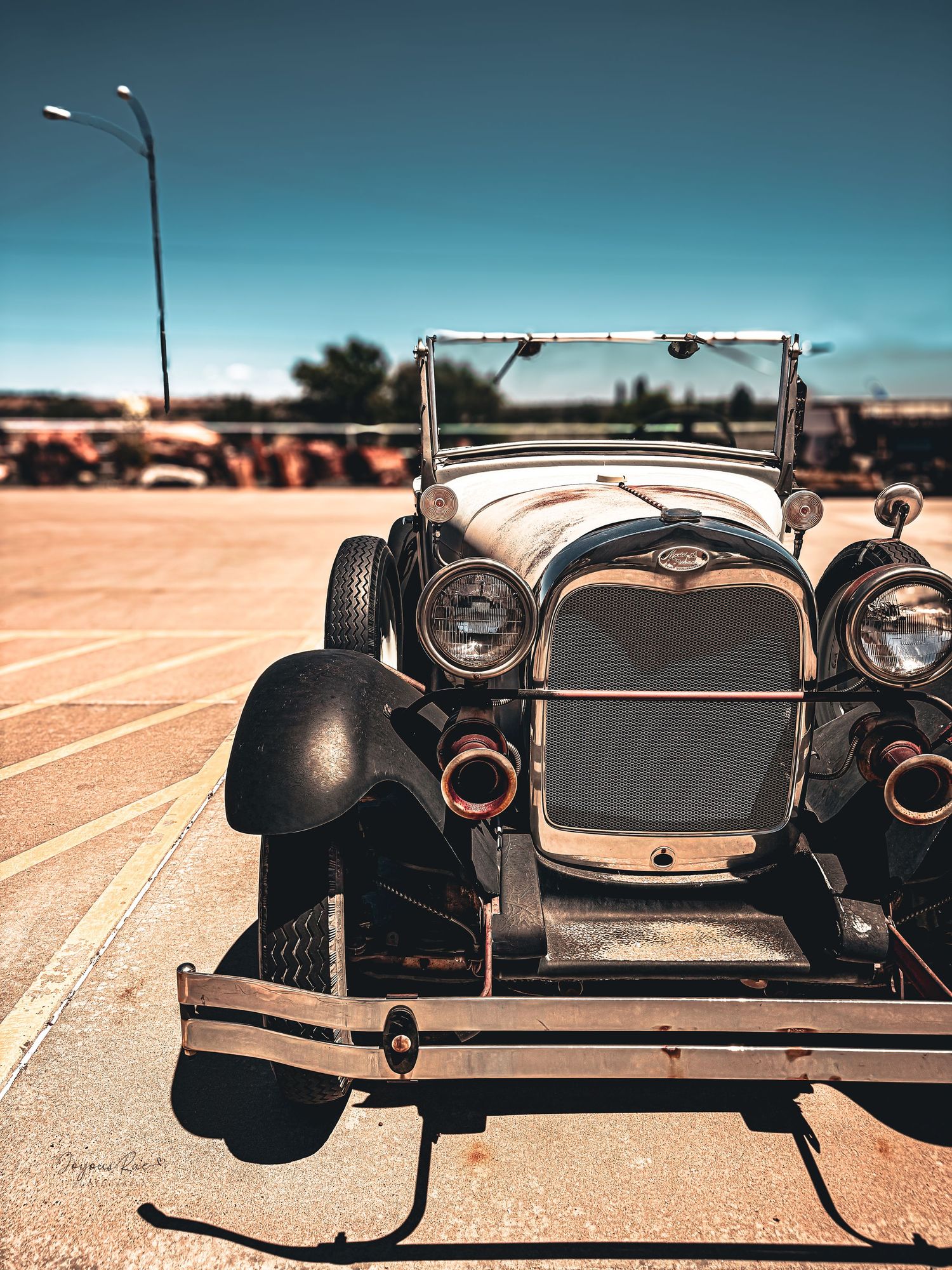 Vintage antique Ford Model A car photographed from the front showing classic chrome headlights and radiator grille in sunny parking lot.