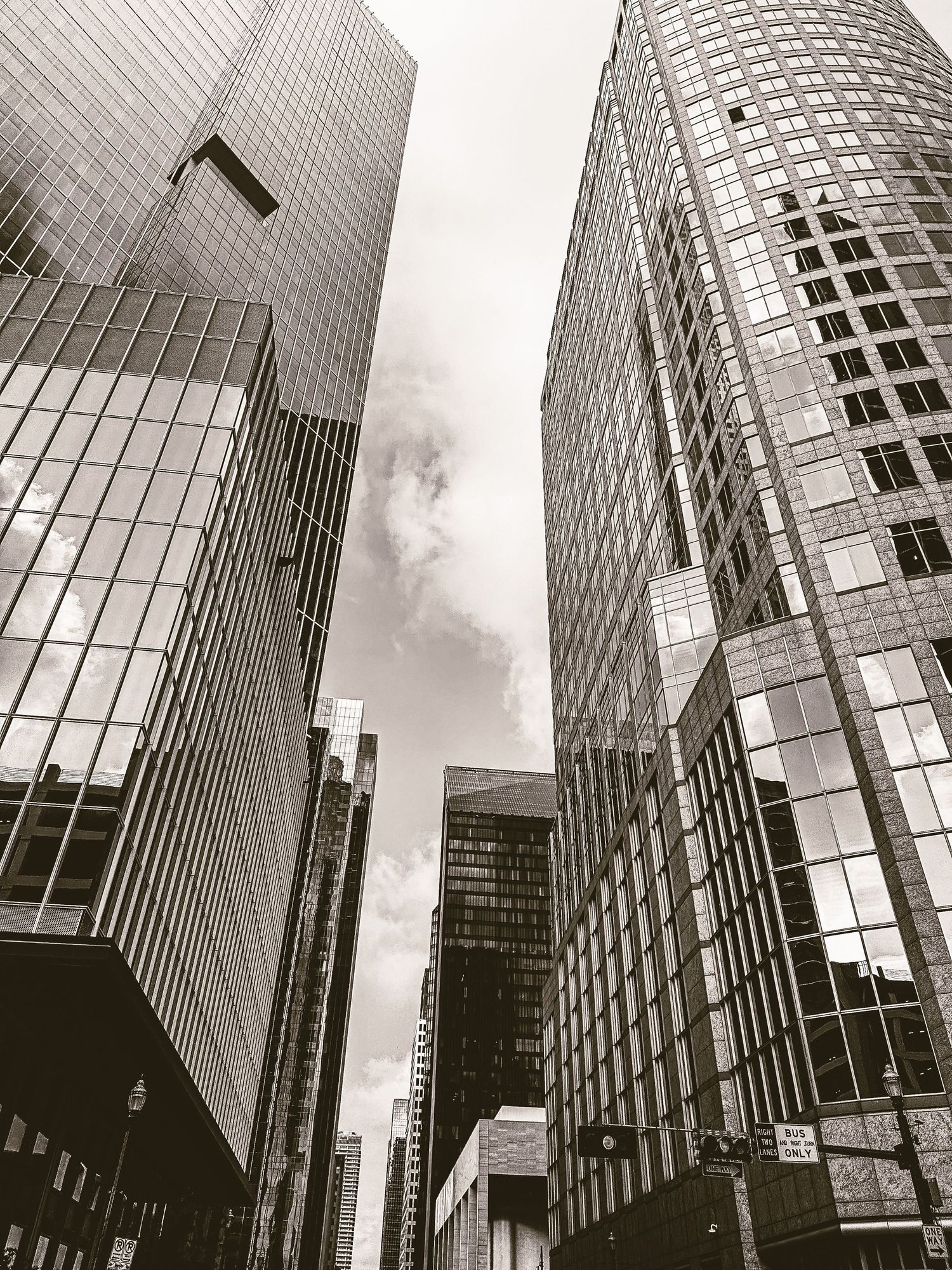 Black and white photo looking up at towering glass skyscrapers against a cloudy sky in a urban city.