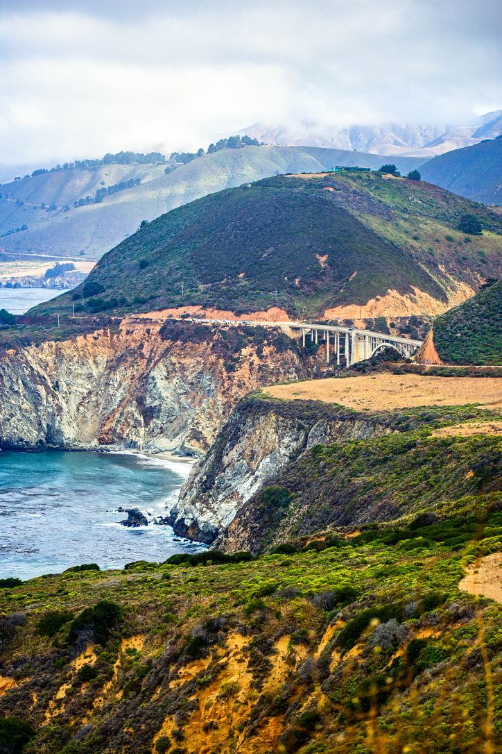 Scenic Big Sur coastline with Bixby Creek Bridge, rugged cliffs, and misty mountains in California.