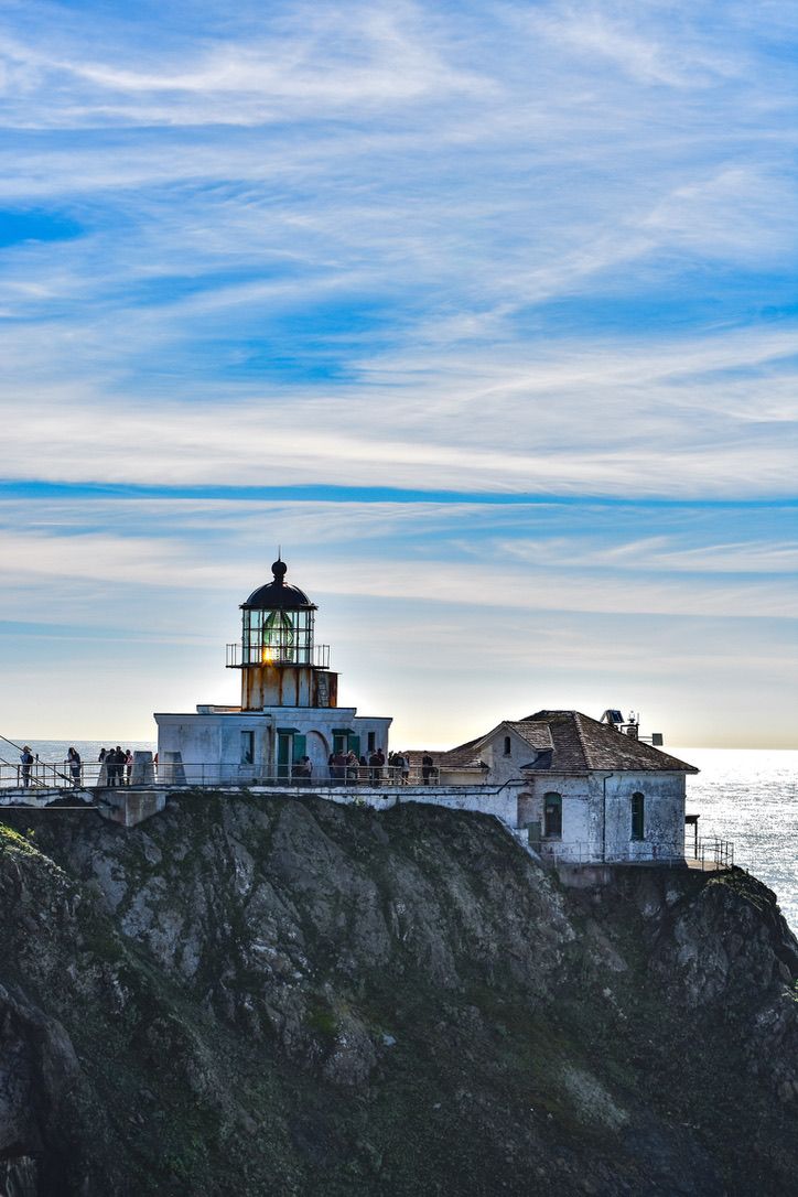 Point Bonita Lighthouse glowing on a rocky cliff overlooking the Pacific Ocean under a blue sky.