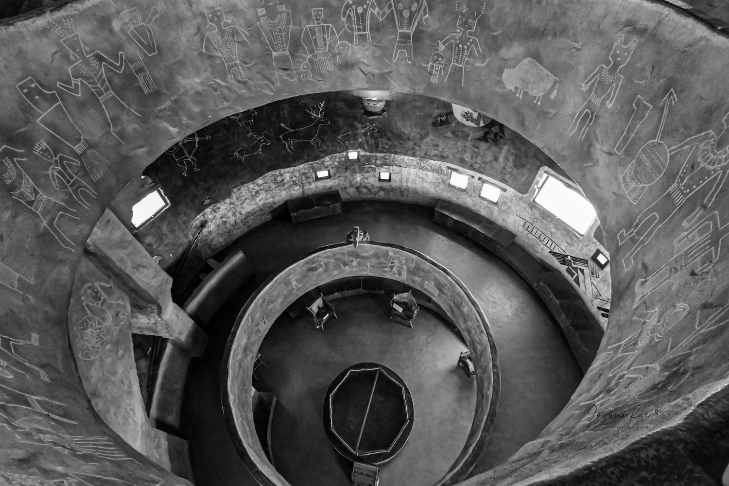 Black and white aerial view of a stunning spiral staircase with ancient wall carvings in a historic building.