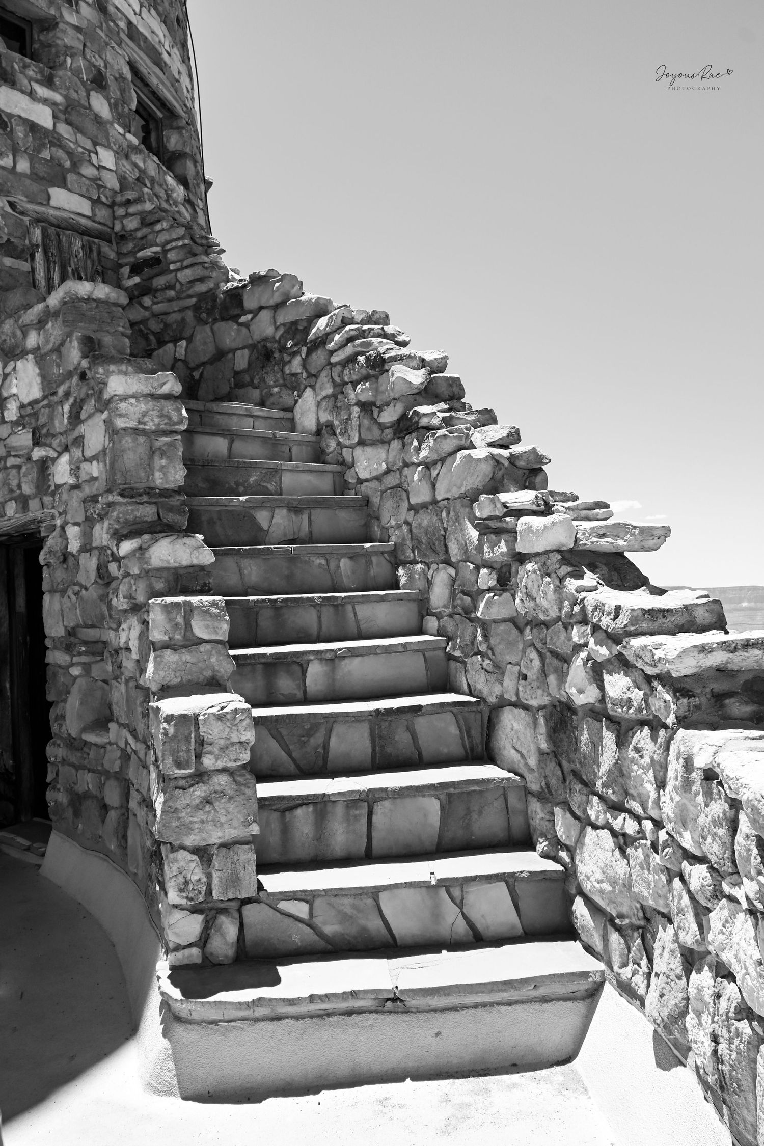 Black and white photo of rustic stone steps along an ancient rock wall structure under bright sunlight.
