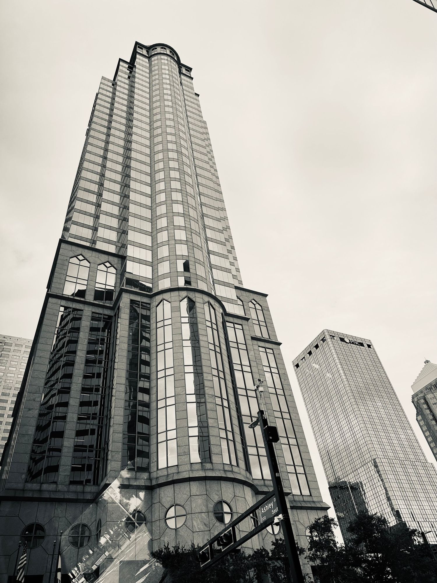 Black and white low-angle view of a tall modern glass skyscraper in a busy city downtown.