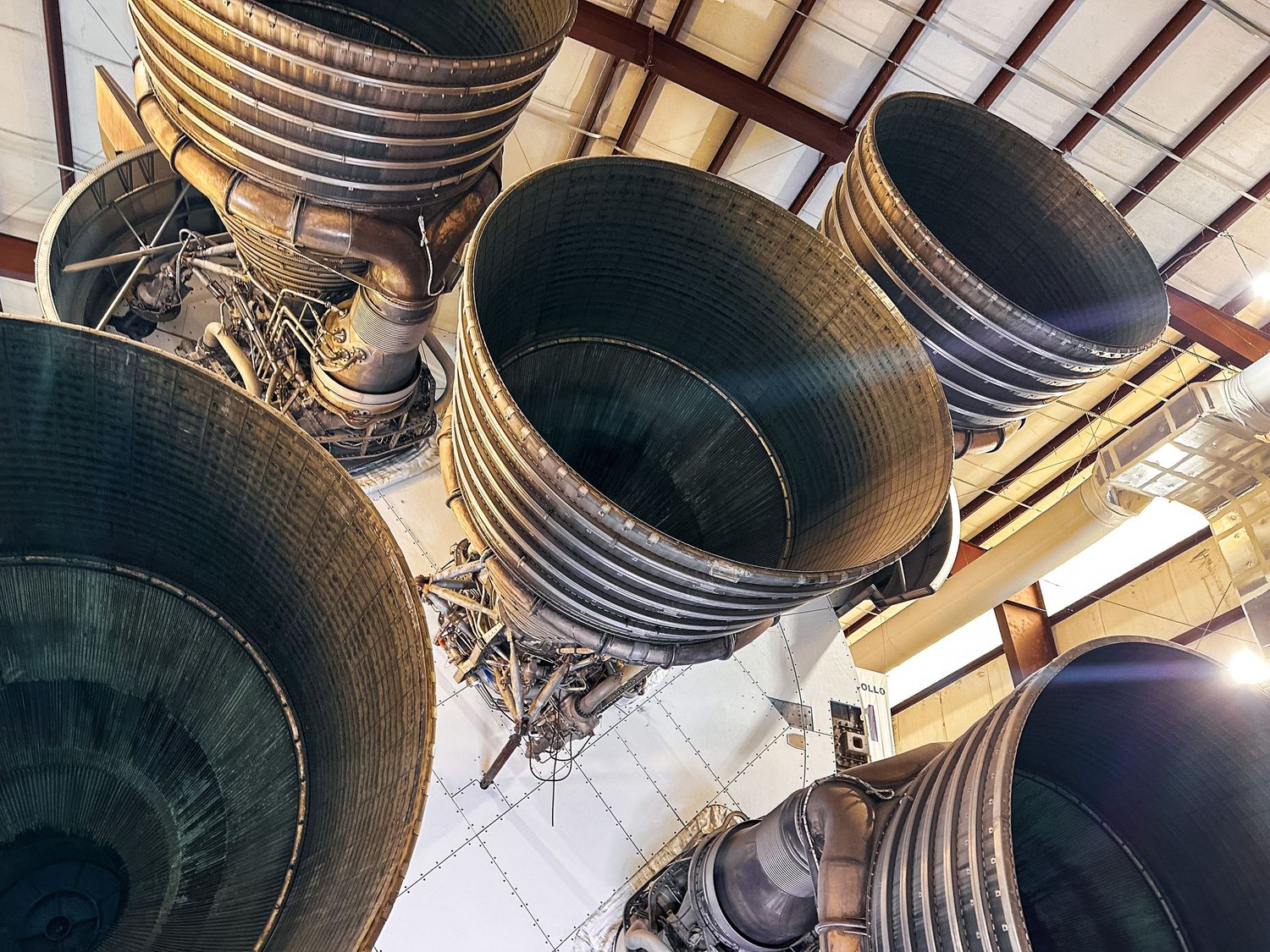 Looking up at massive rocket engine nozzles of a Saturn V rocket on display indoors.