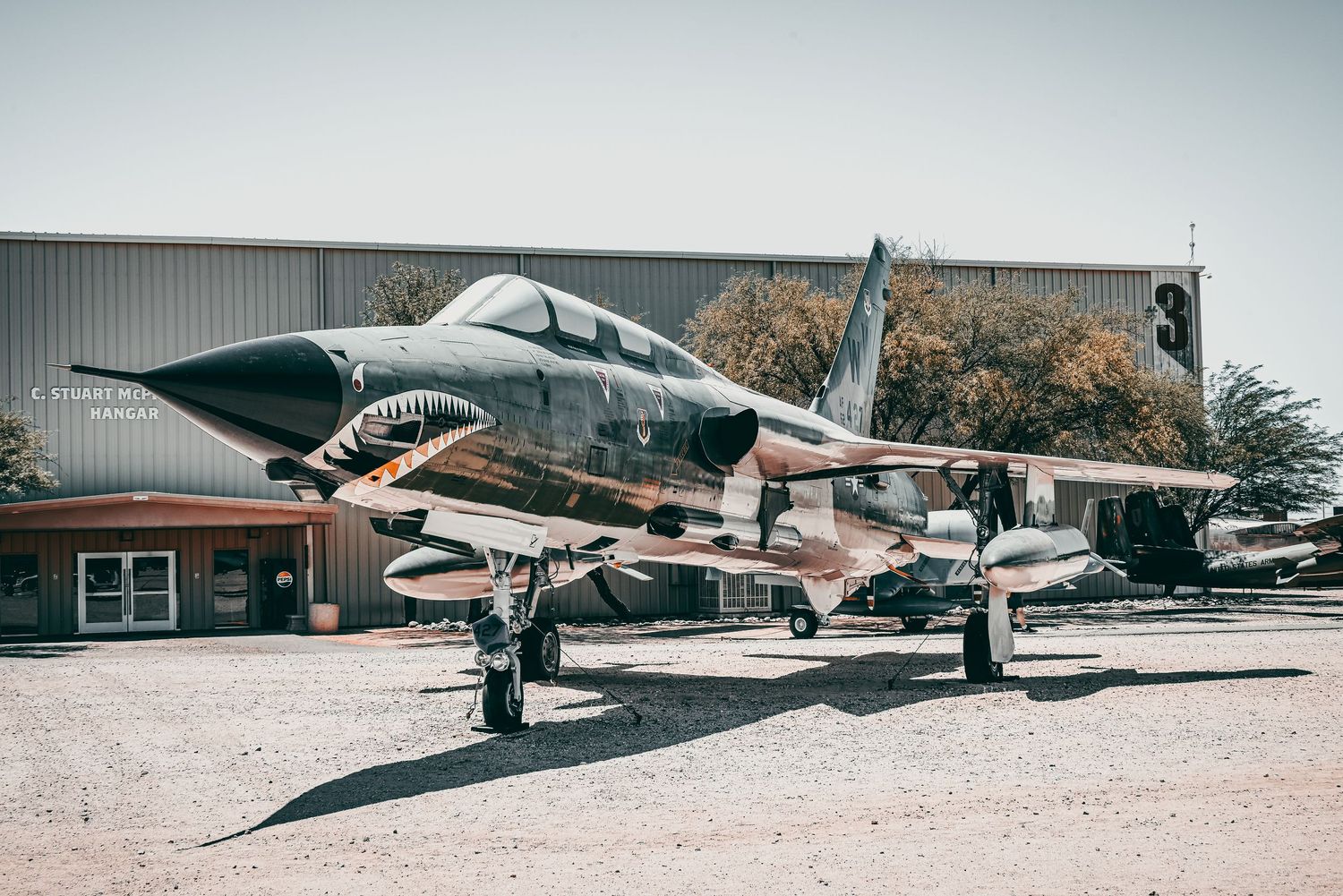 Military jet fighter with shark mouth nose art displayed outdoors at an aviation museum.