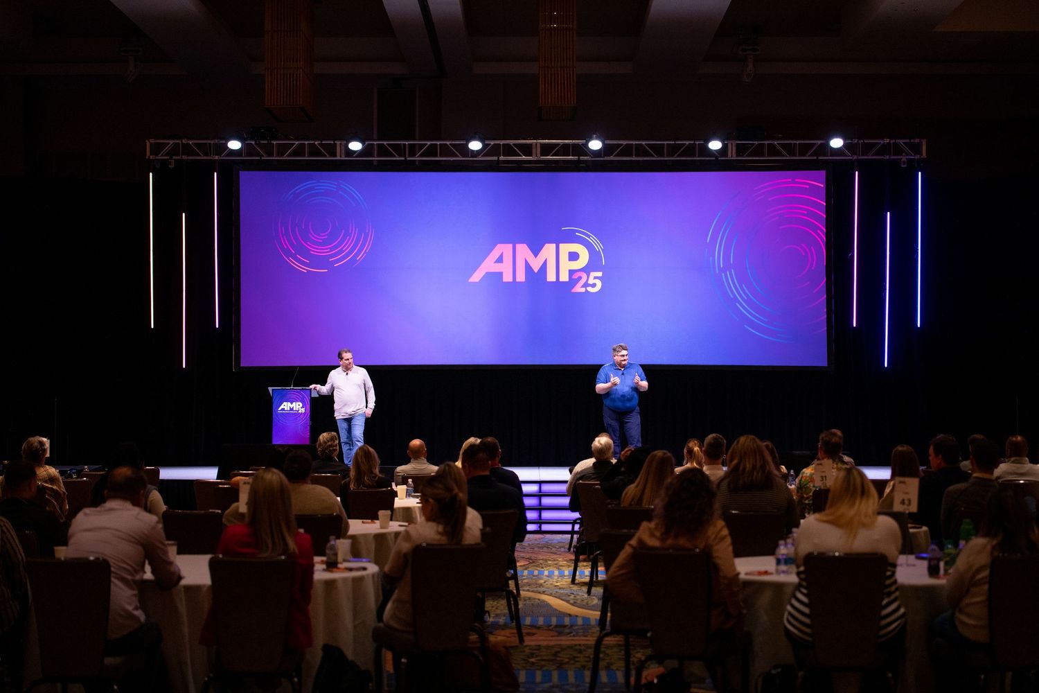 Stage with digital designs on a screen at a Sales Kick Off meeting with people in the audience watching.